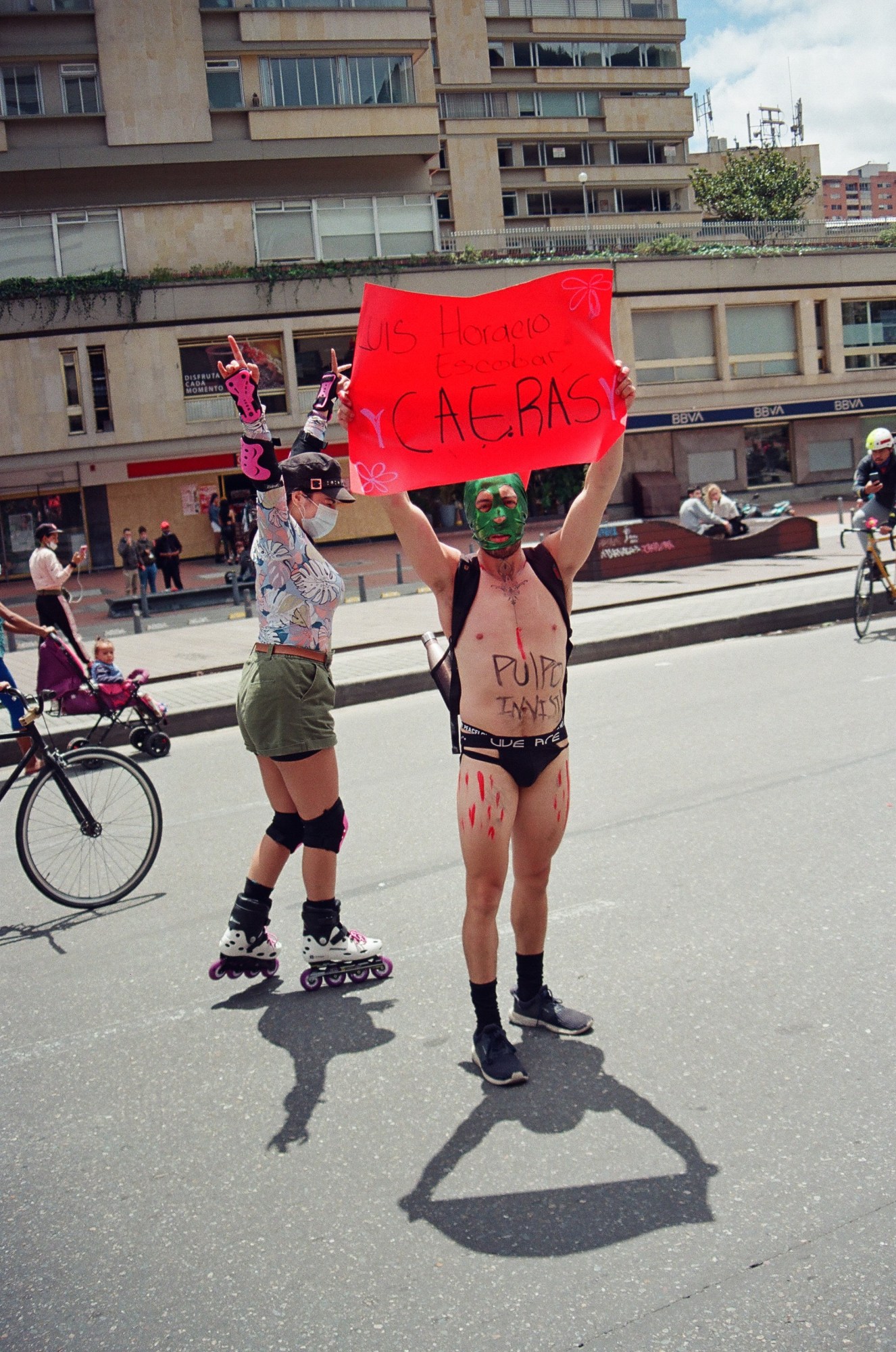 a colombian protester wearing a mask and holding a sign up in the street