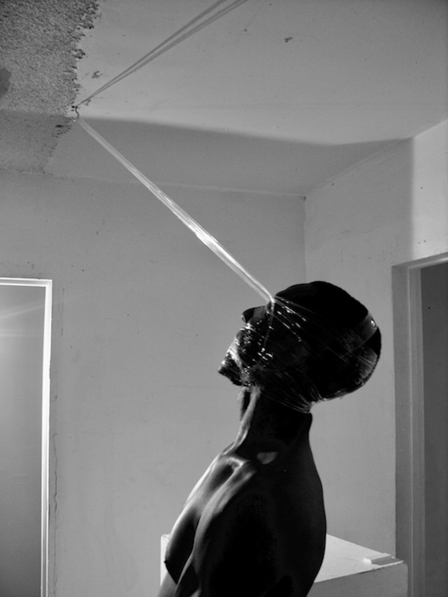 a topless man with tape wrapped around his head that is attached to a hook on the ceiling