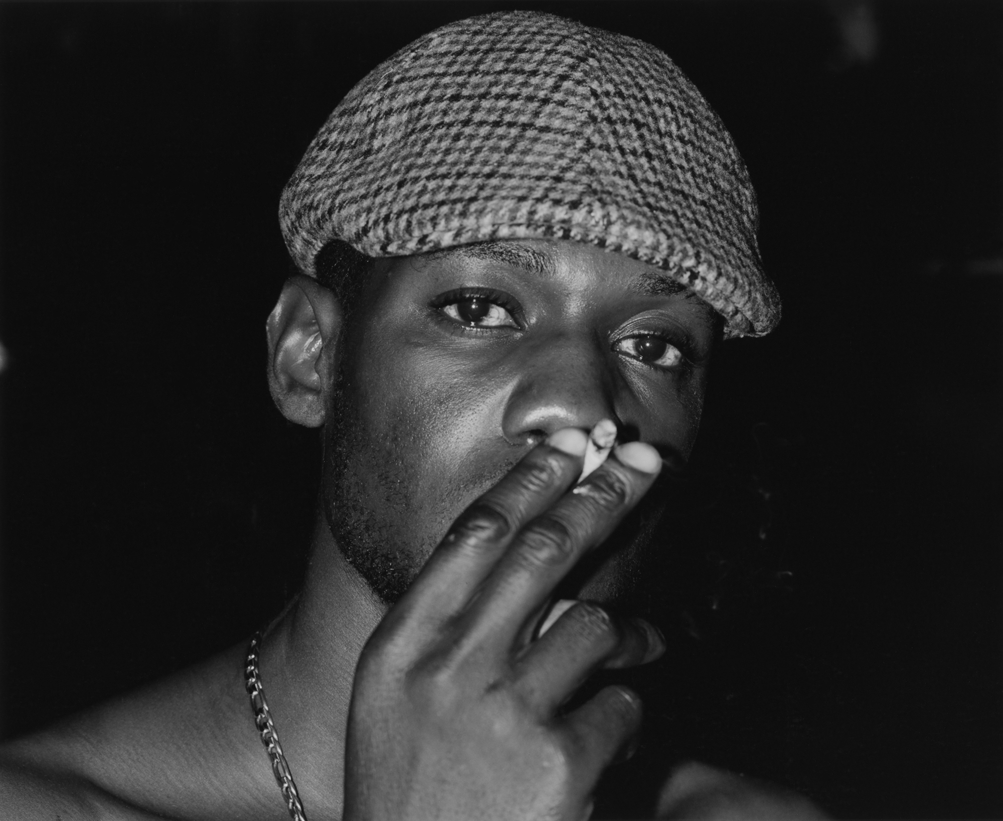 a man in a hat stares into the camera and smokes