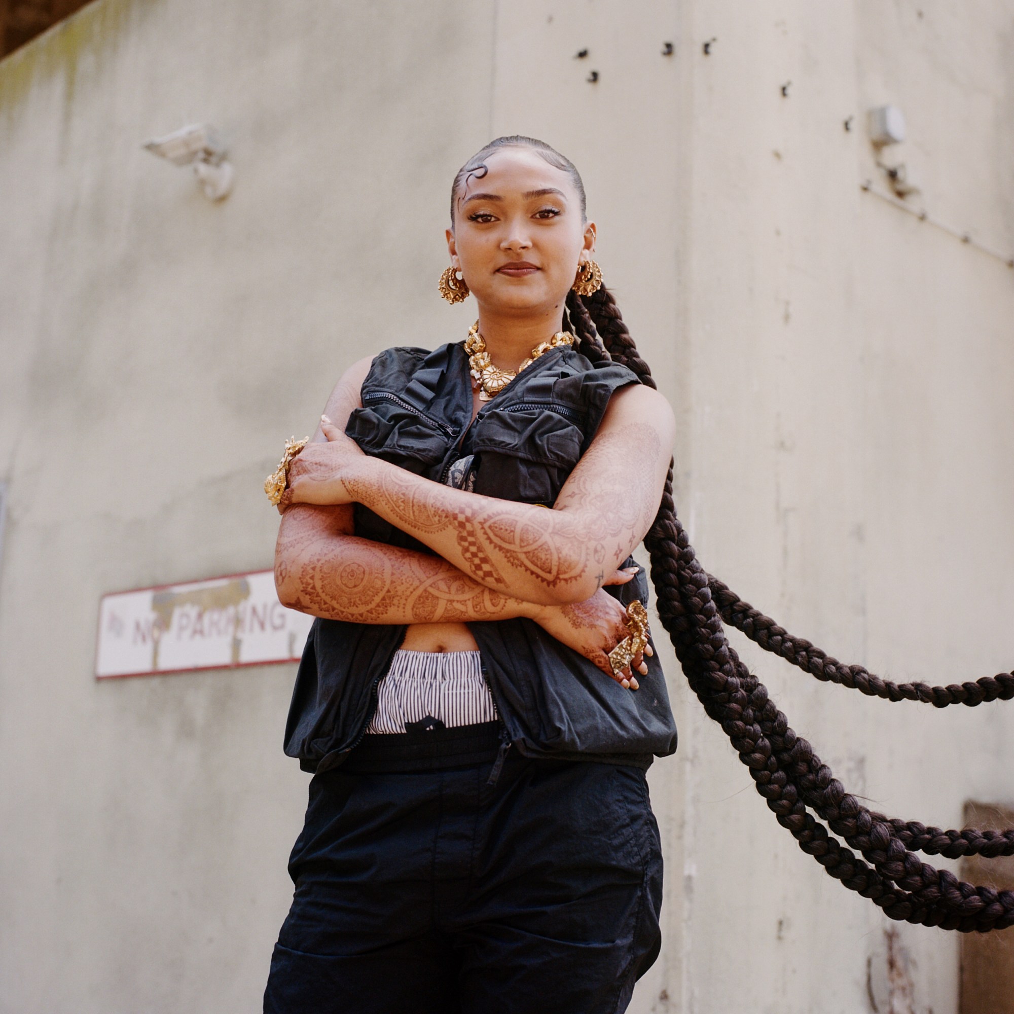 a woman in a vest jacket with henna tattoos, gold jewellery and long braided hair