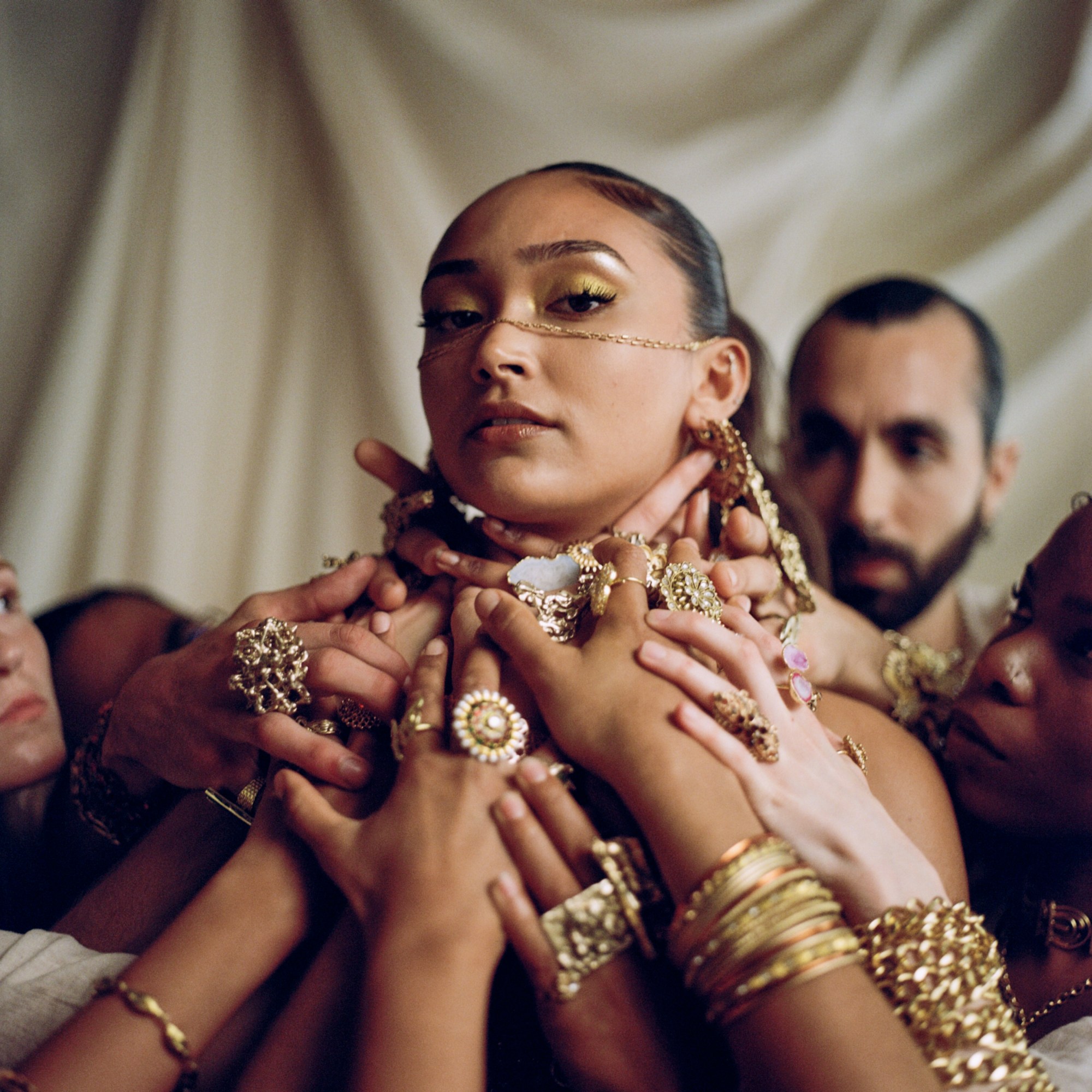 the singer joy crookes surrounded by hands covered in gold jewellery