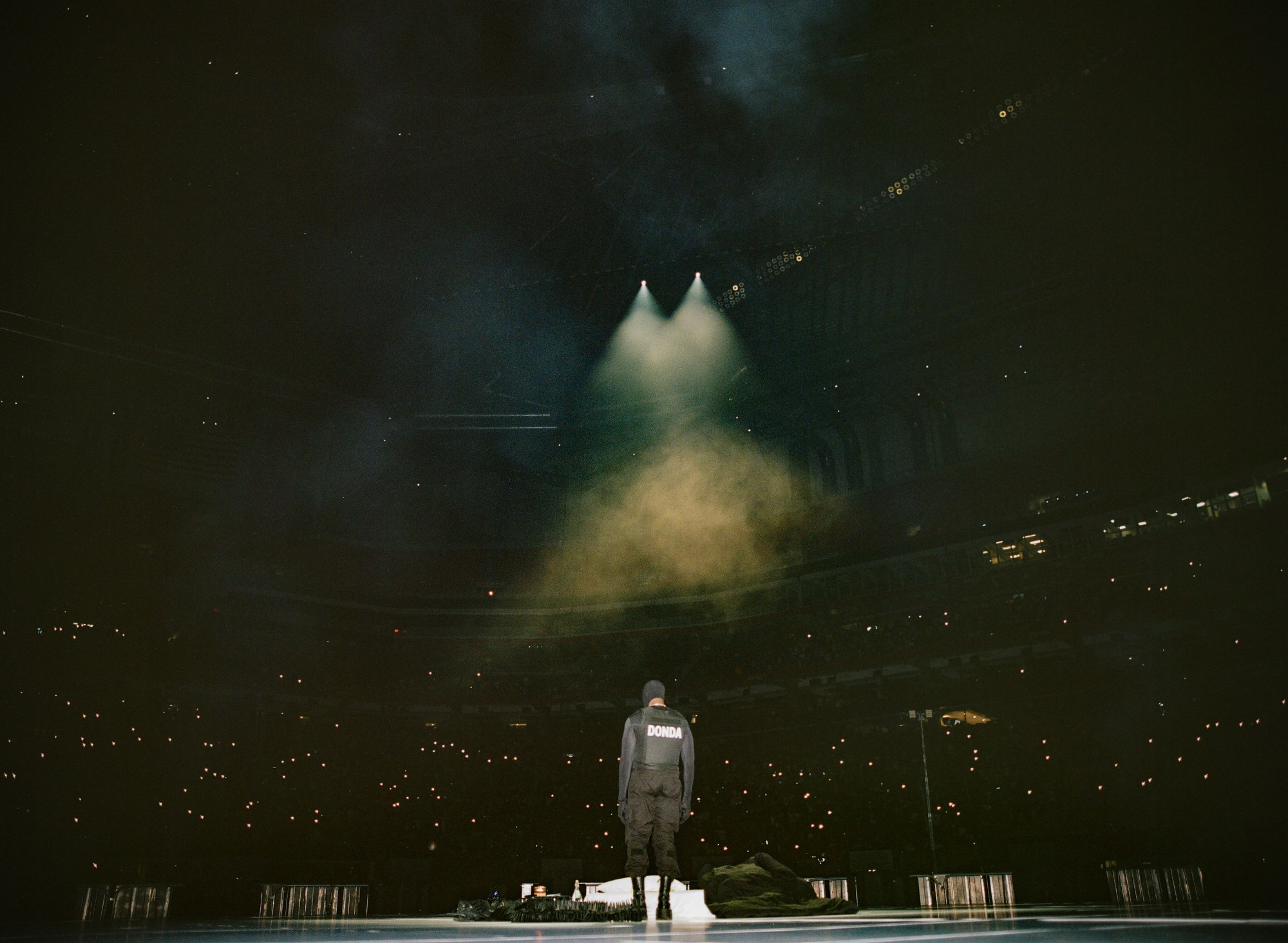 Kanye west looking out to the crowd at his donda show dressed in bulletproof vest and mask