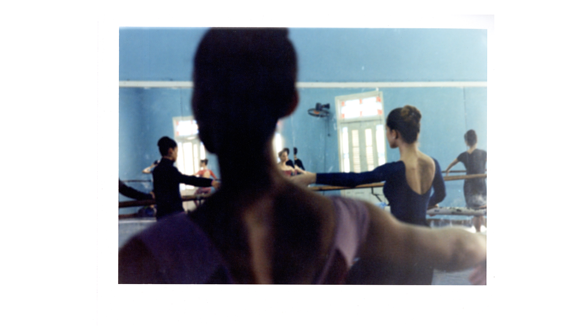 a photograph, shot from behind a dancer's head, captures a busy rehearsal room