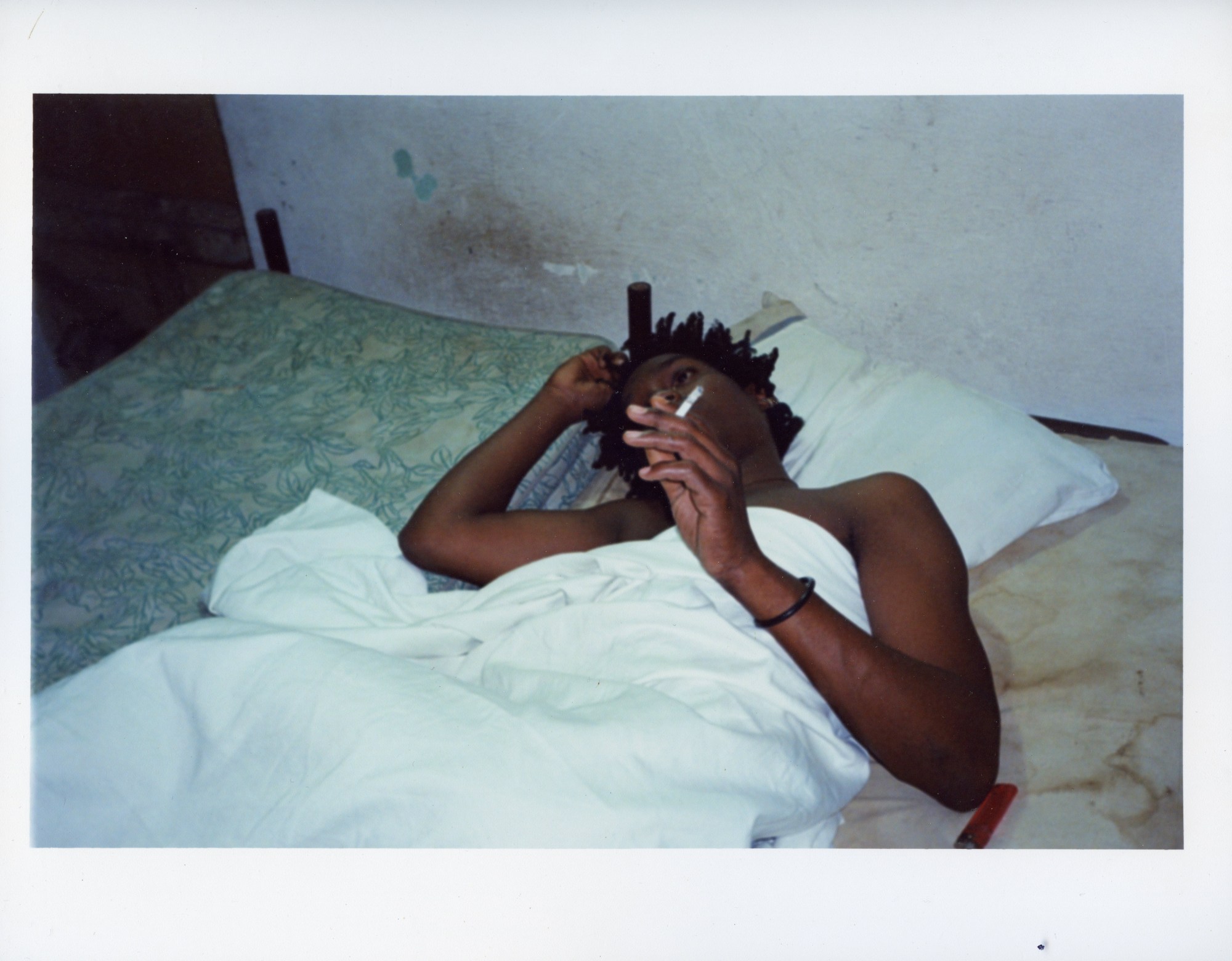 a topless man lying in bed smoking a cigarette