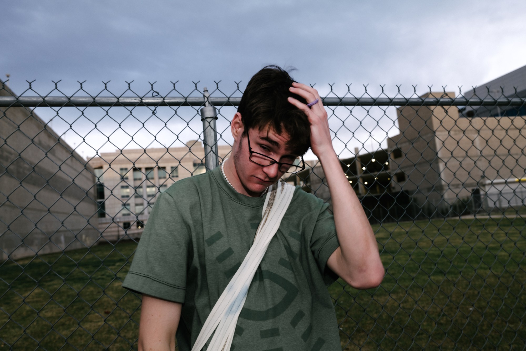 giles standing in front of a chainlink fence with his hand on his head by blake lewis