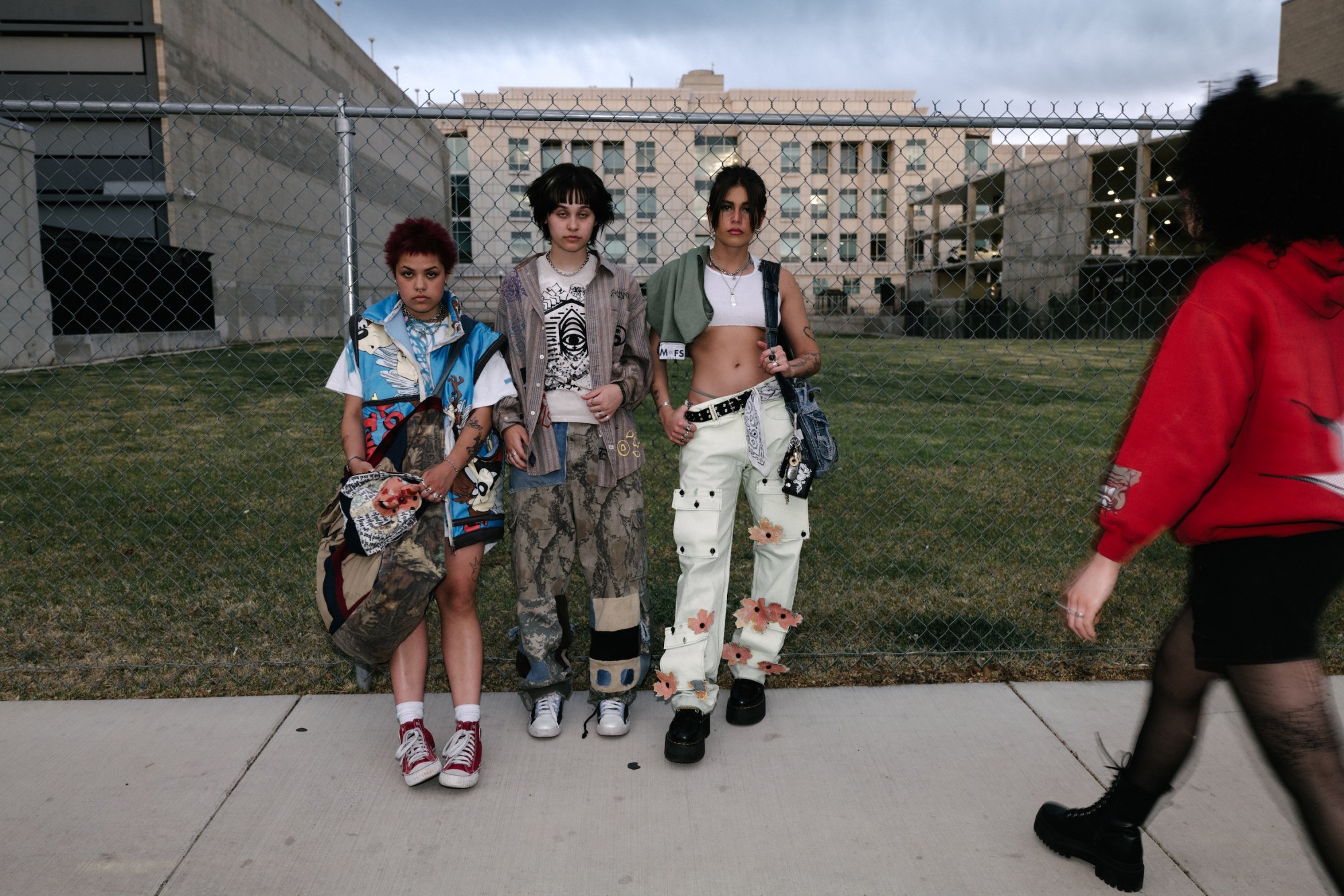 three girls wearing upcycled clothes standing in front of a chainlink fence by blake lewis