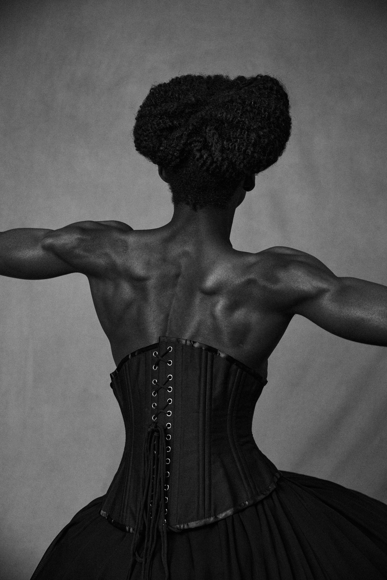 a muscular man in a corset shot from behind in black and white