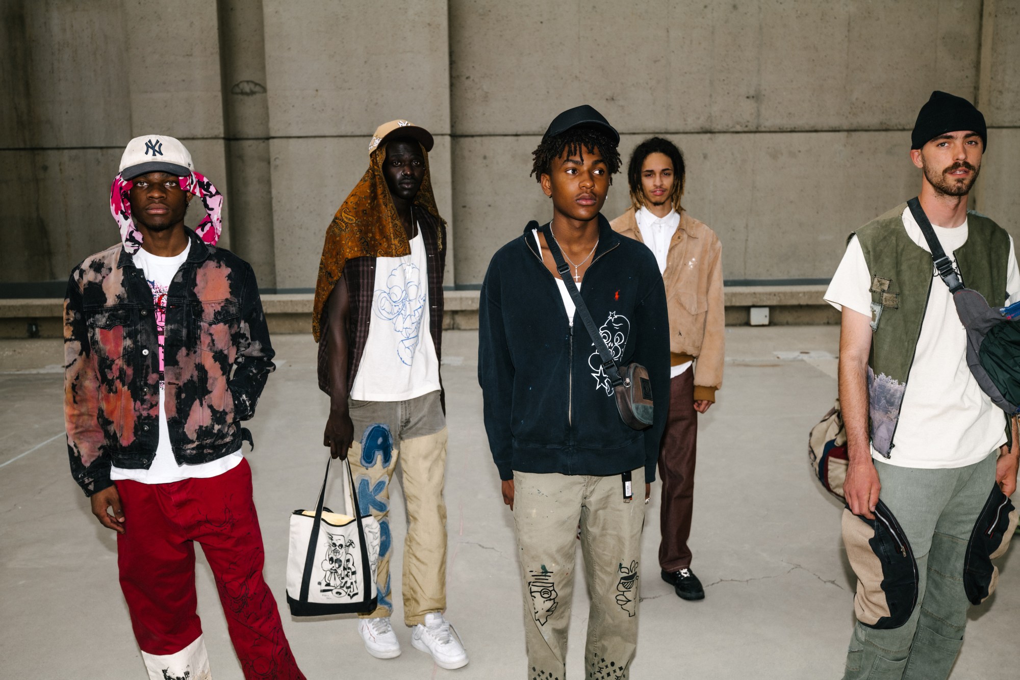 a group of teens in upcycled clothes standing in front of a cement wall by blake lewis