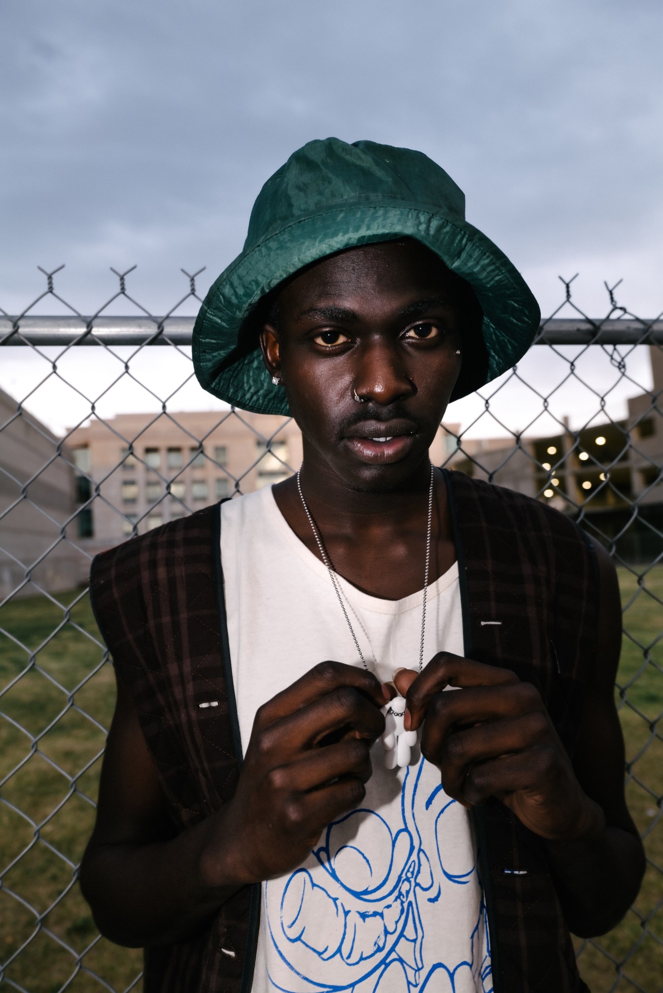 portrait of a boy in a bucket hat standing in front of a chainlink fence by blake lewis