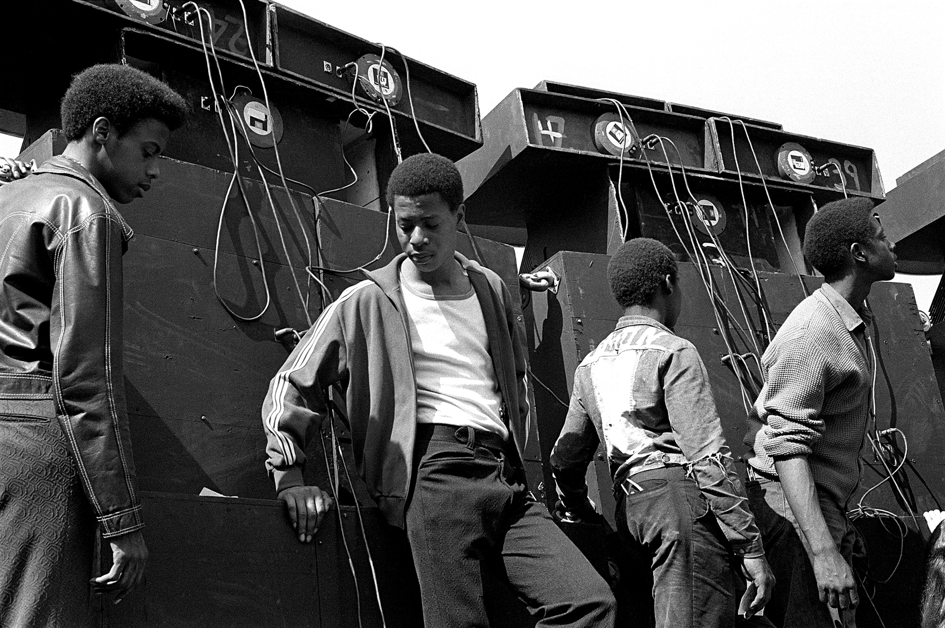 four men in similar outfits in front of large boxes with wires hanging out