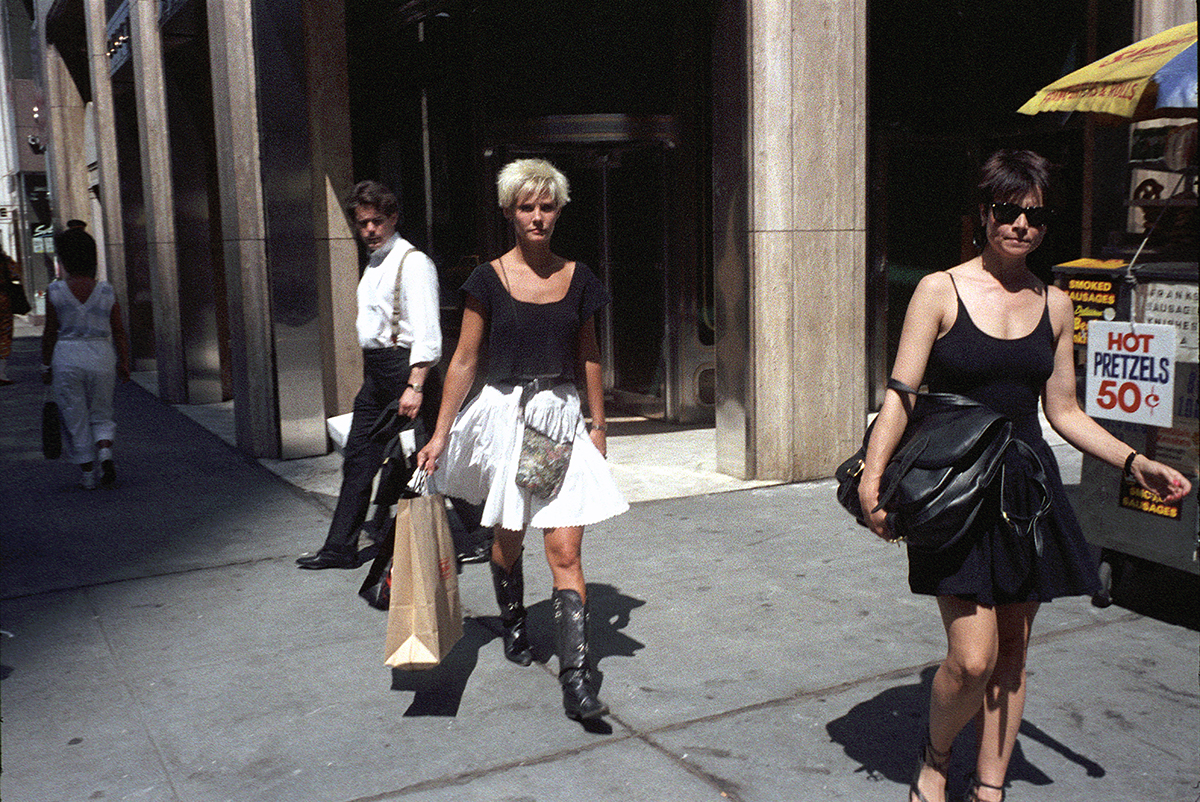 two women walking on the street, one to the left wearing cowboy boots and a white skirt