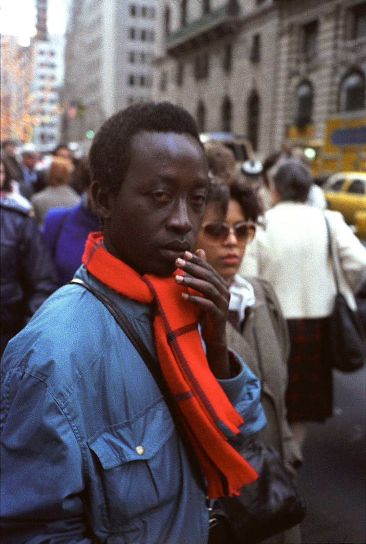 a man in a blue jacket and red scarf holds his hand to his mouth