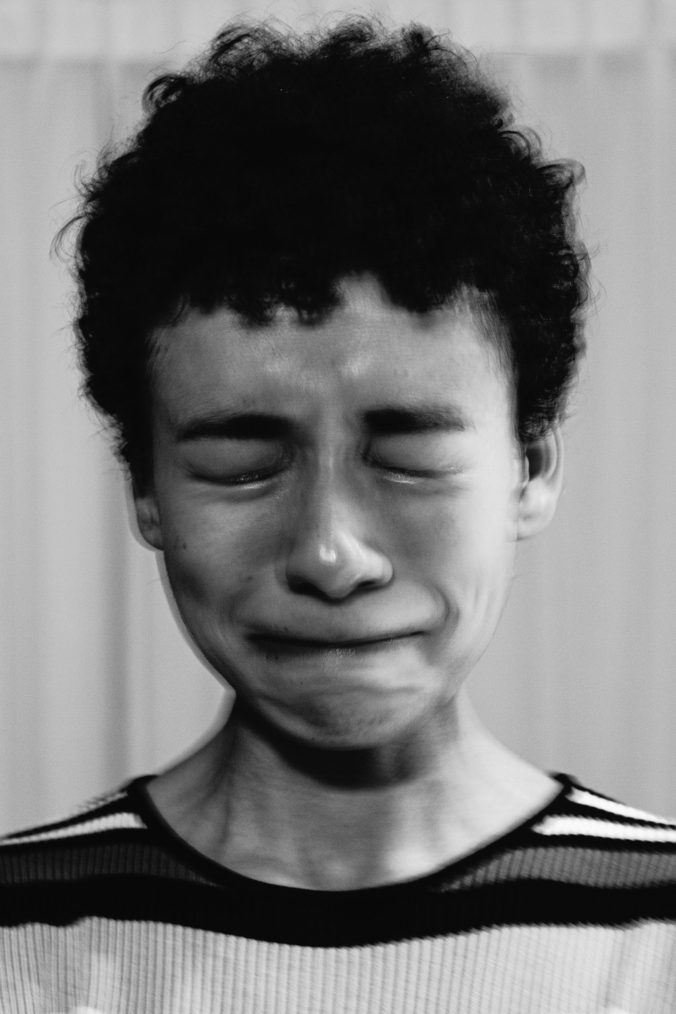 a person in a stripy jumper clenching their face and crying