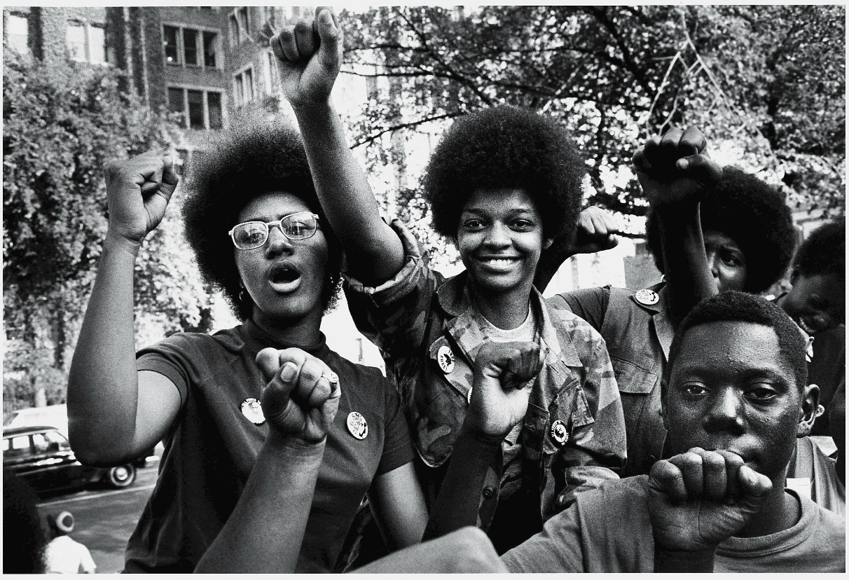 Three Black women raise their fists in the air at a demonstration in the 1970s