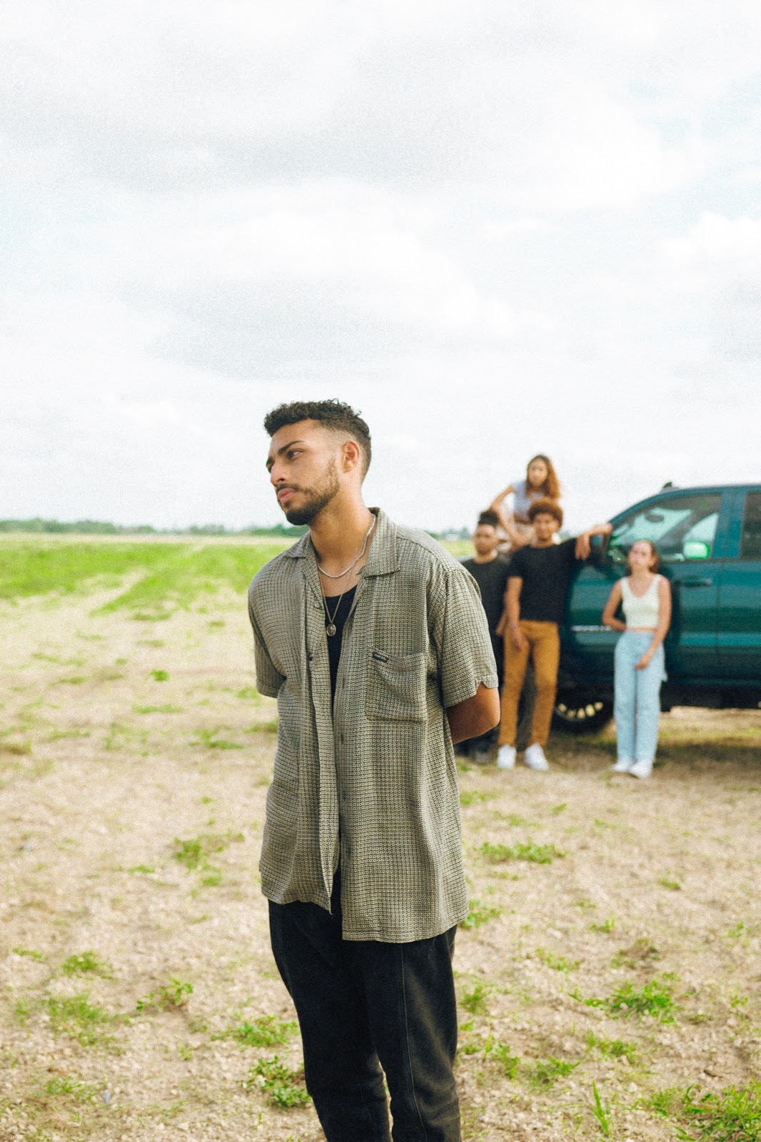 marco g standing in a field looking off with a truck and people behind him