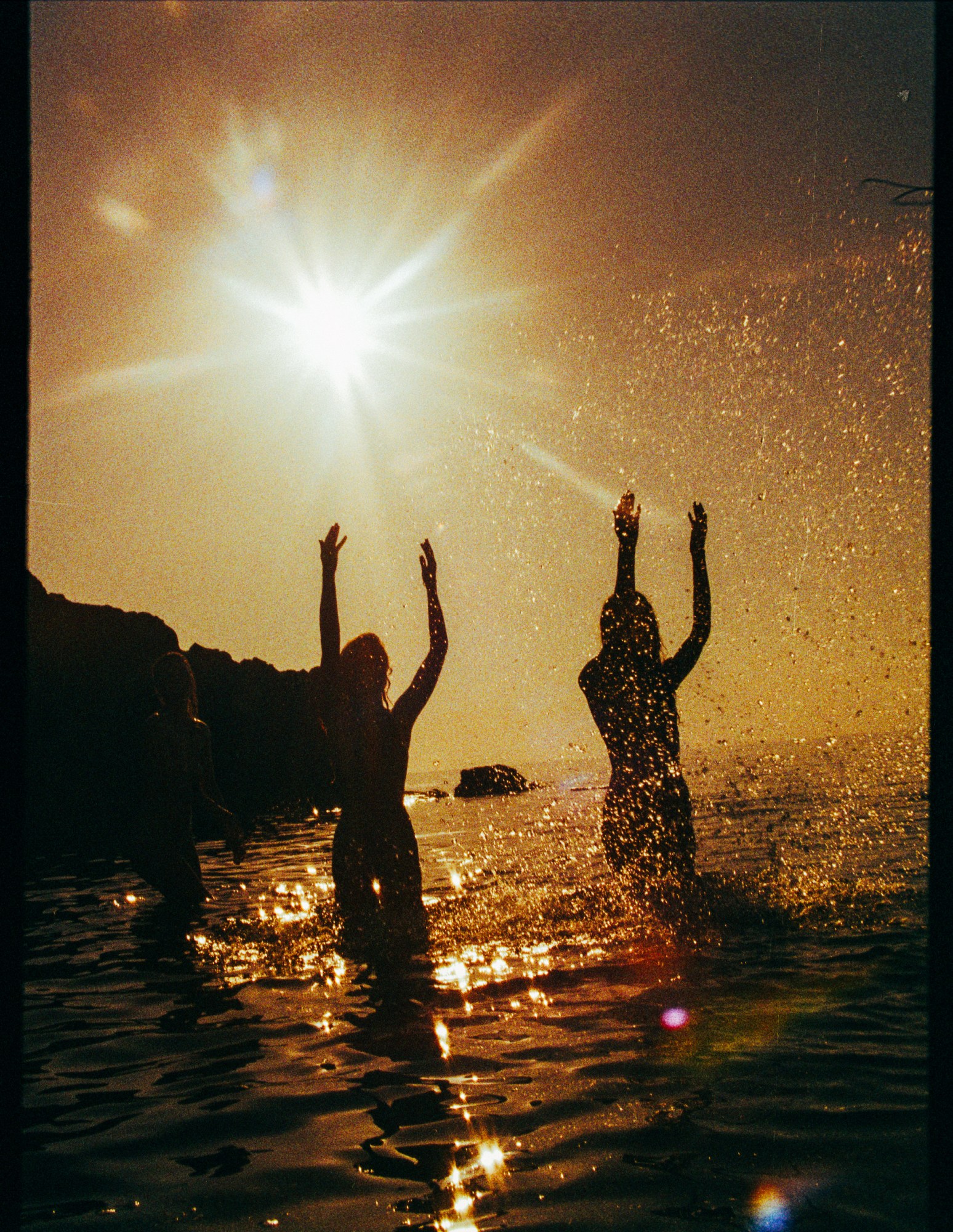 two girls naked in the ocean at sunset