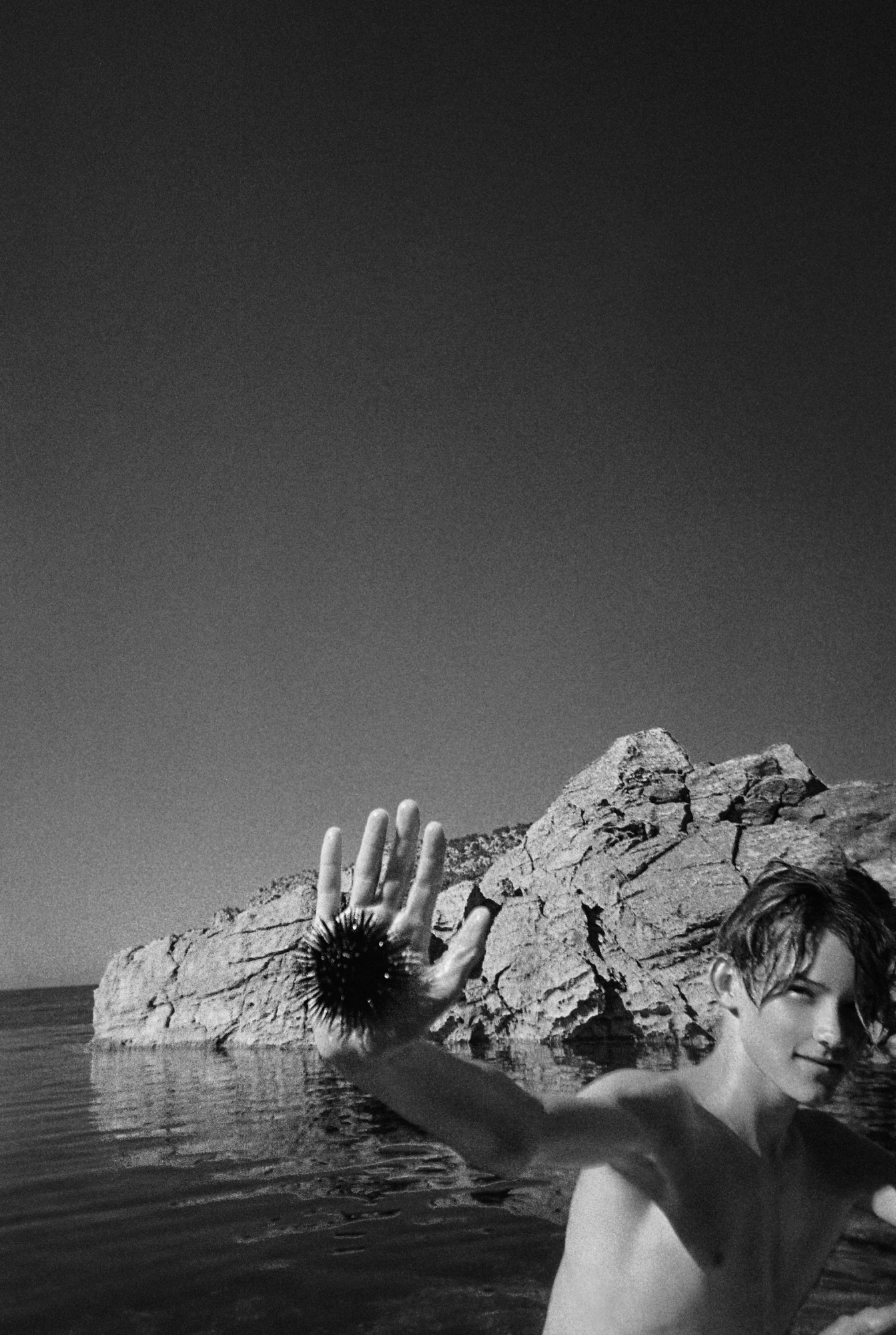 a black and white portrait of a boy holding up a sea urchin