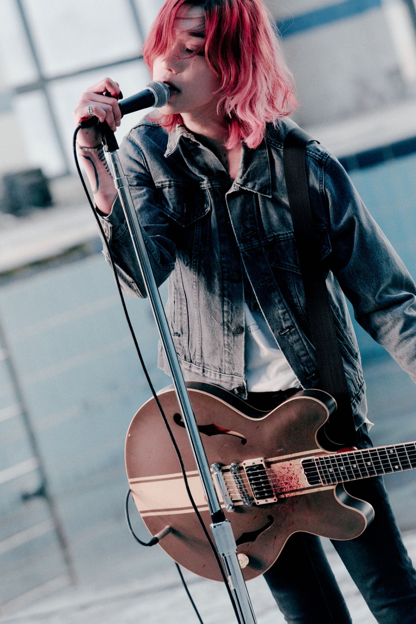 South Korean musician LØREN, with long pink hair and a blood-splattered guitar, sings into a microphone