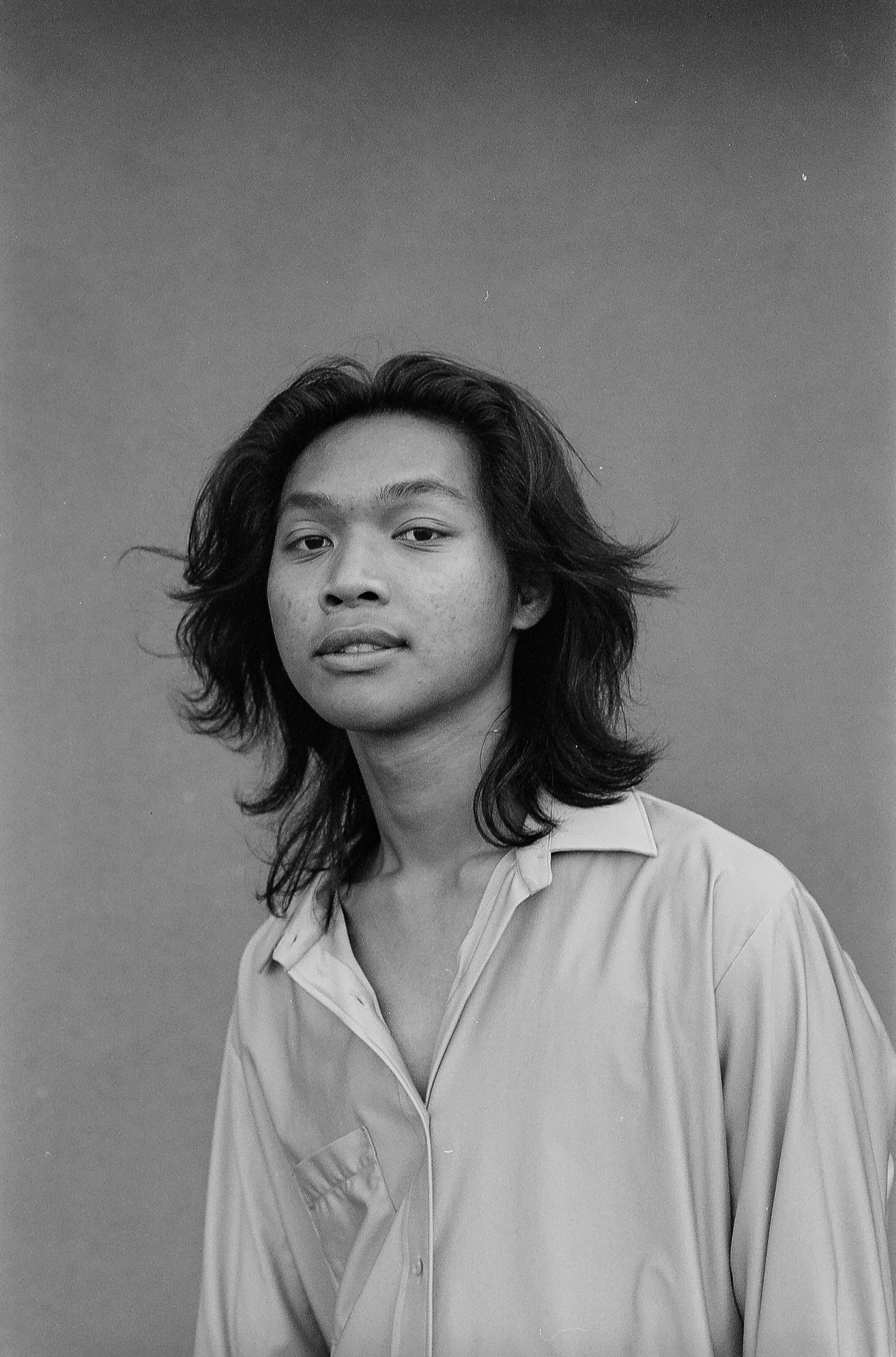 Black and white portrait of a man wearing an open satin shirt with his hair blowing back.