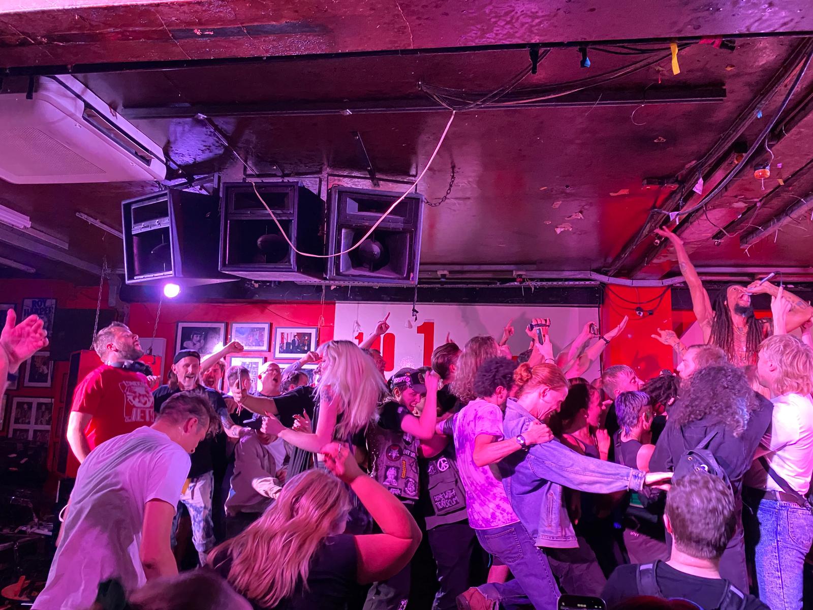 A mosh pit scene at a concert under pink and purple lights.