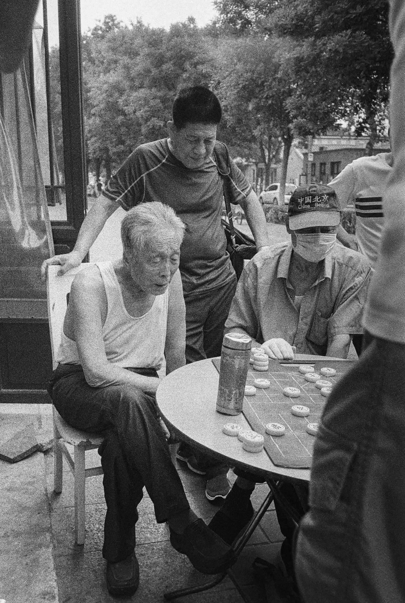 A group of people play chess on a table outside.