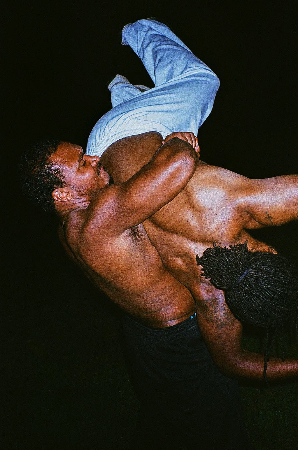 Two men wrestle shirtless in the dark