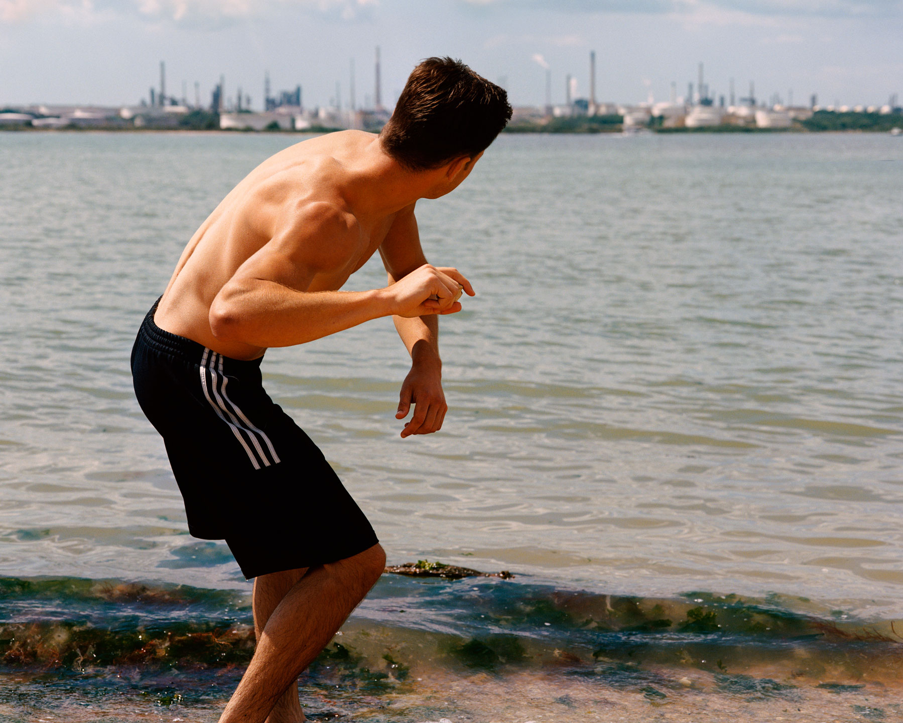 a topless young man wearing Adidas shorts skims stones