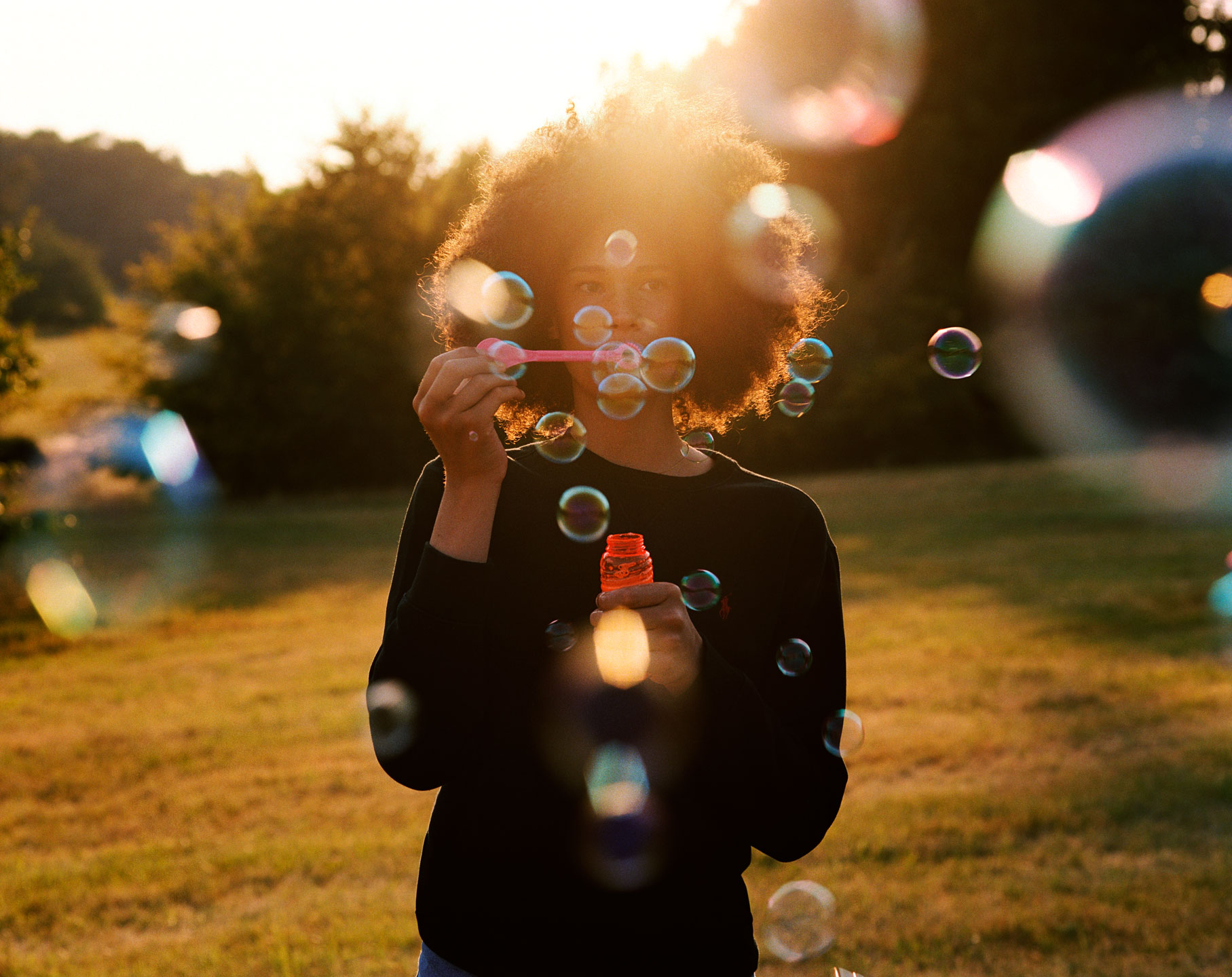 a woman with an afro blows bubbles in the golden hour light