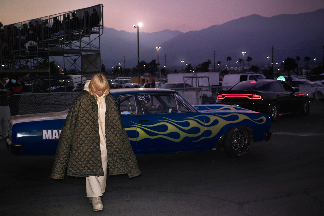 billie eilish in a racing car track at sunset wearing an oversized coat