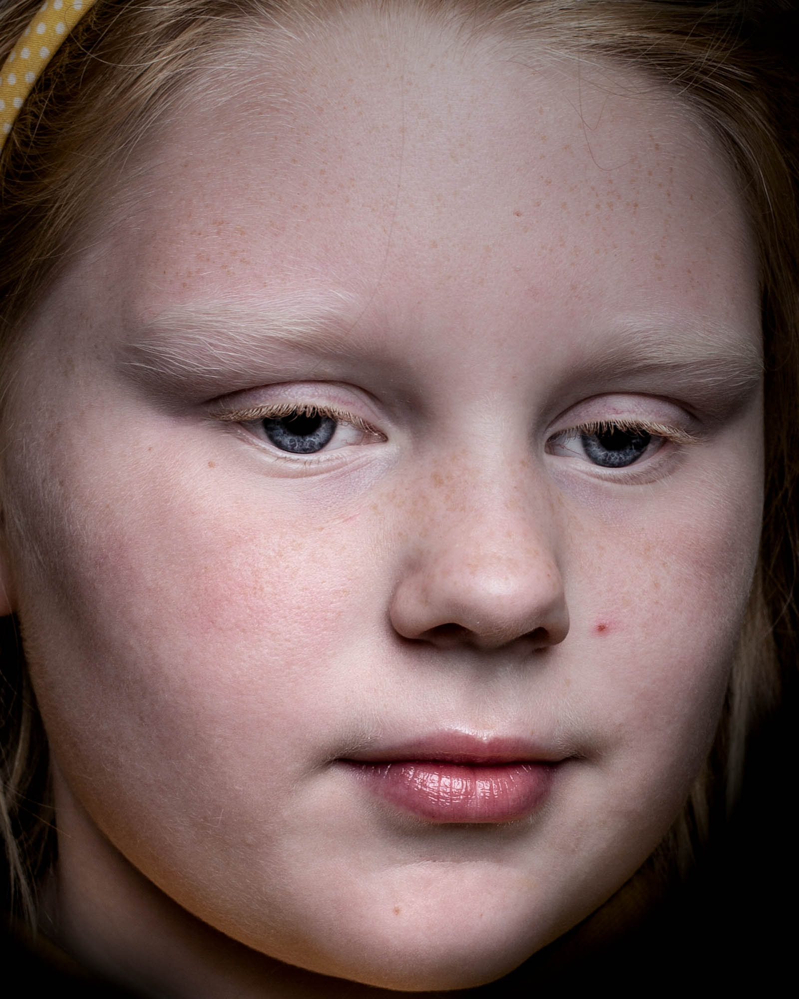 a close-up of a young woman's face, wearing a yellow alice band on her hair