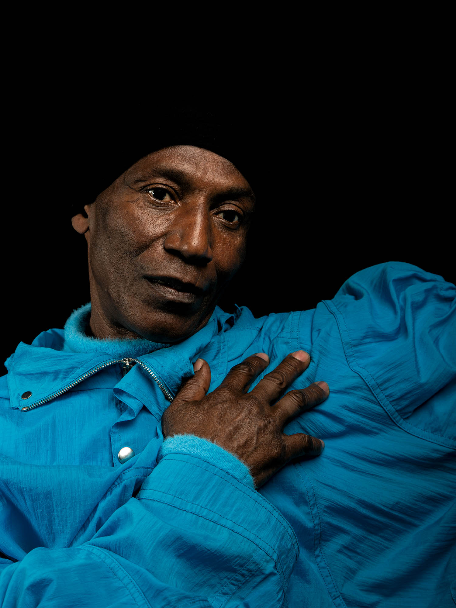 an older man wearing a bright blue jacket against a black backdrop