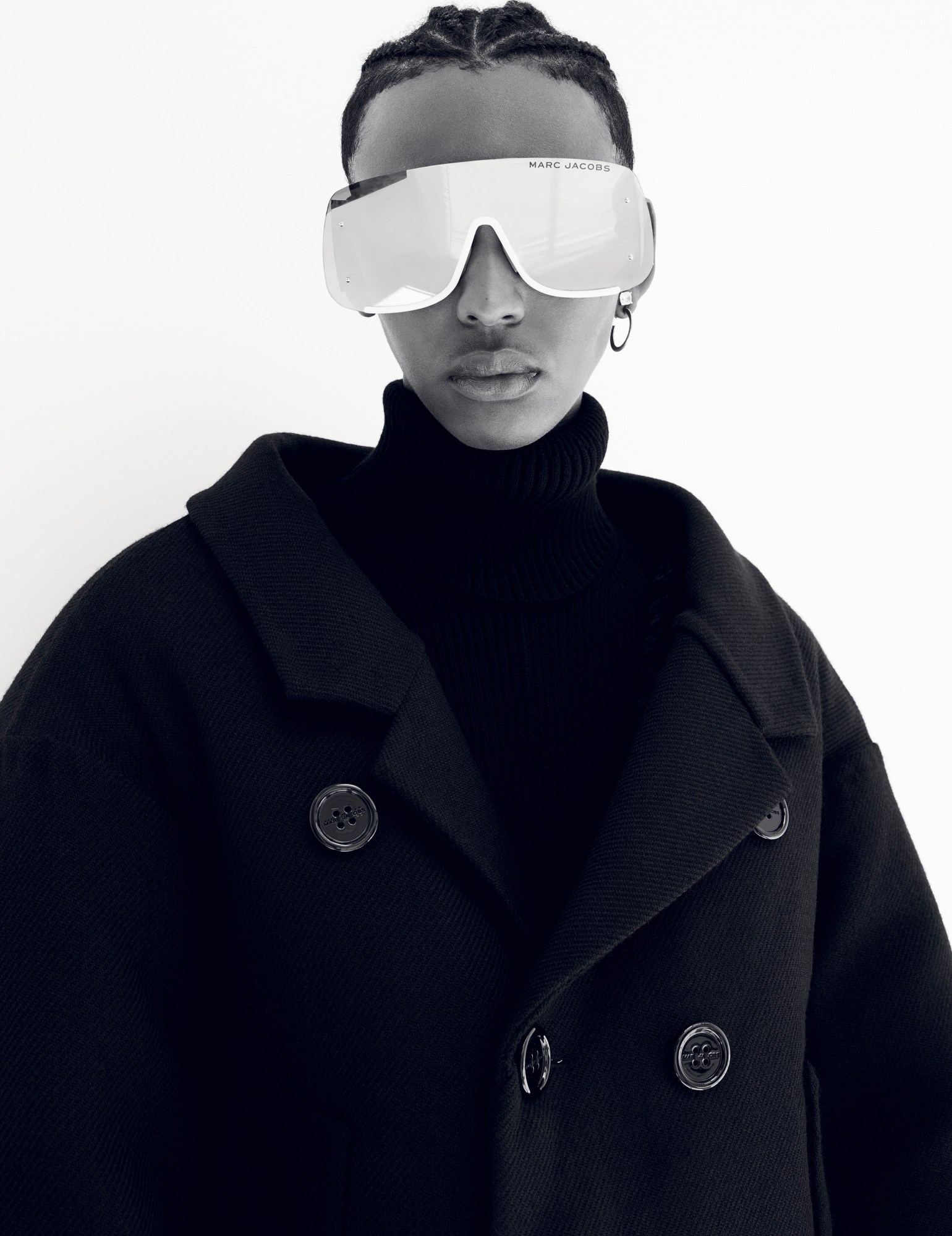 a model in a black overcoat and rollneck sweater wears oversized reflective sunglasses