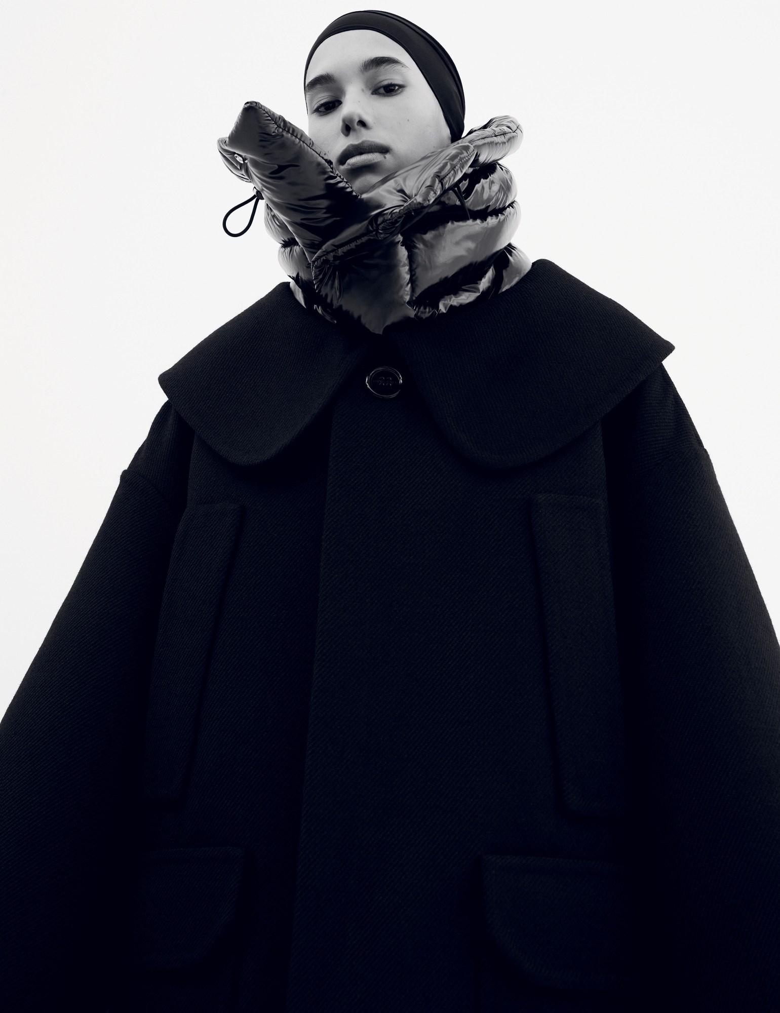 a model with a head covering wears a dark felt coat over a puffer jacket seen at the neck