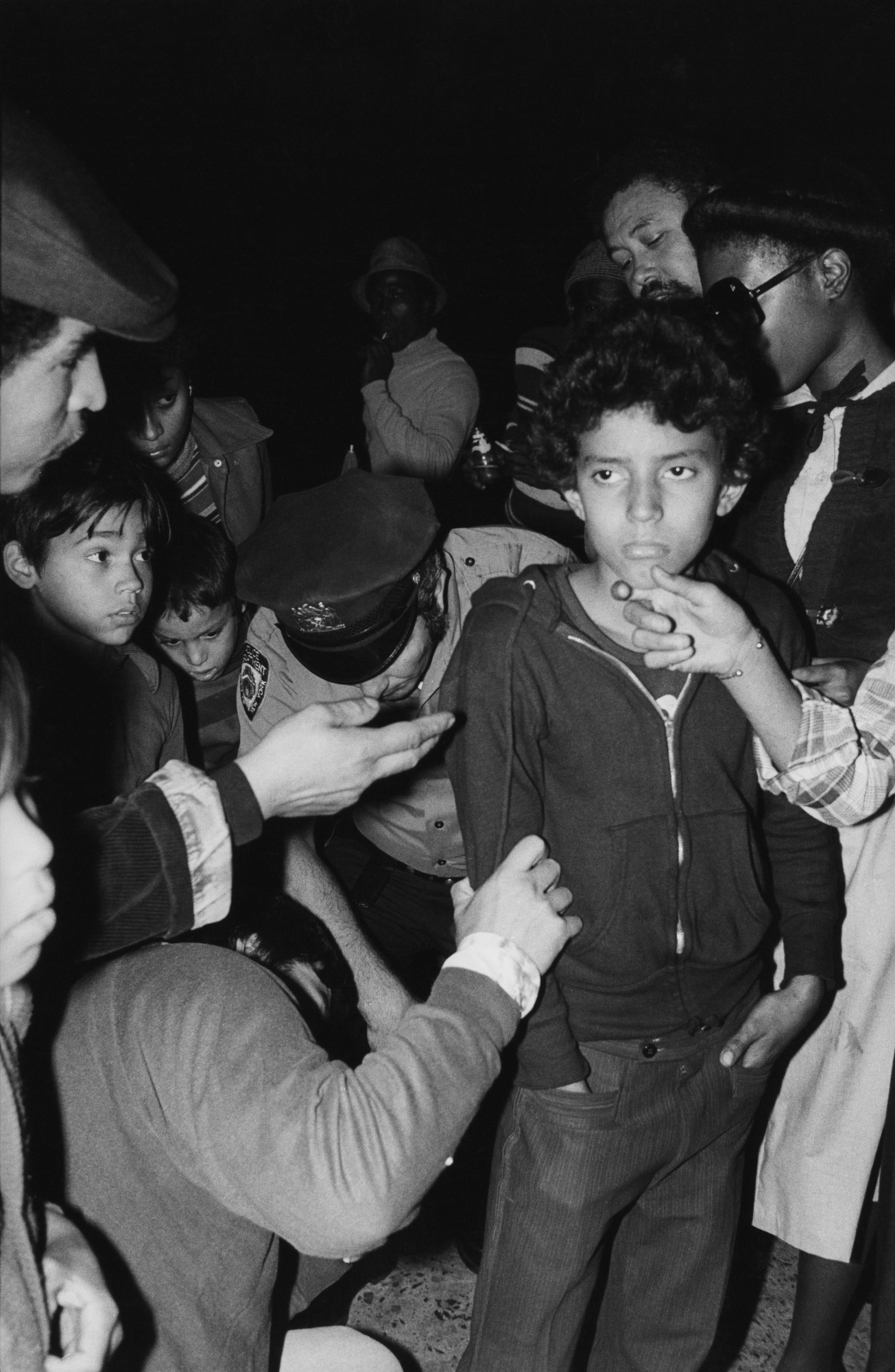 a policeman searches a young kid surrounded by people