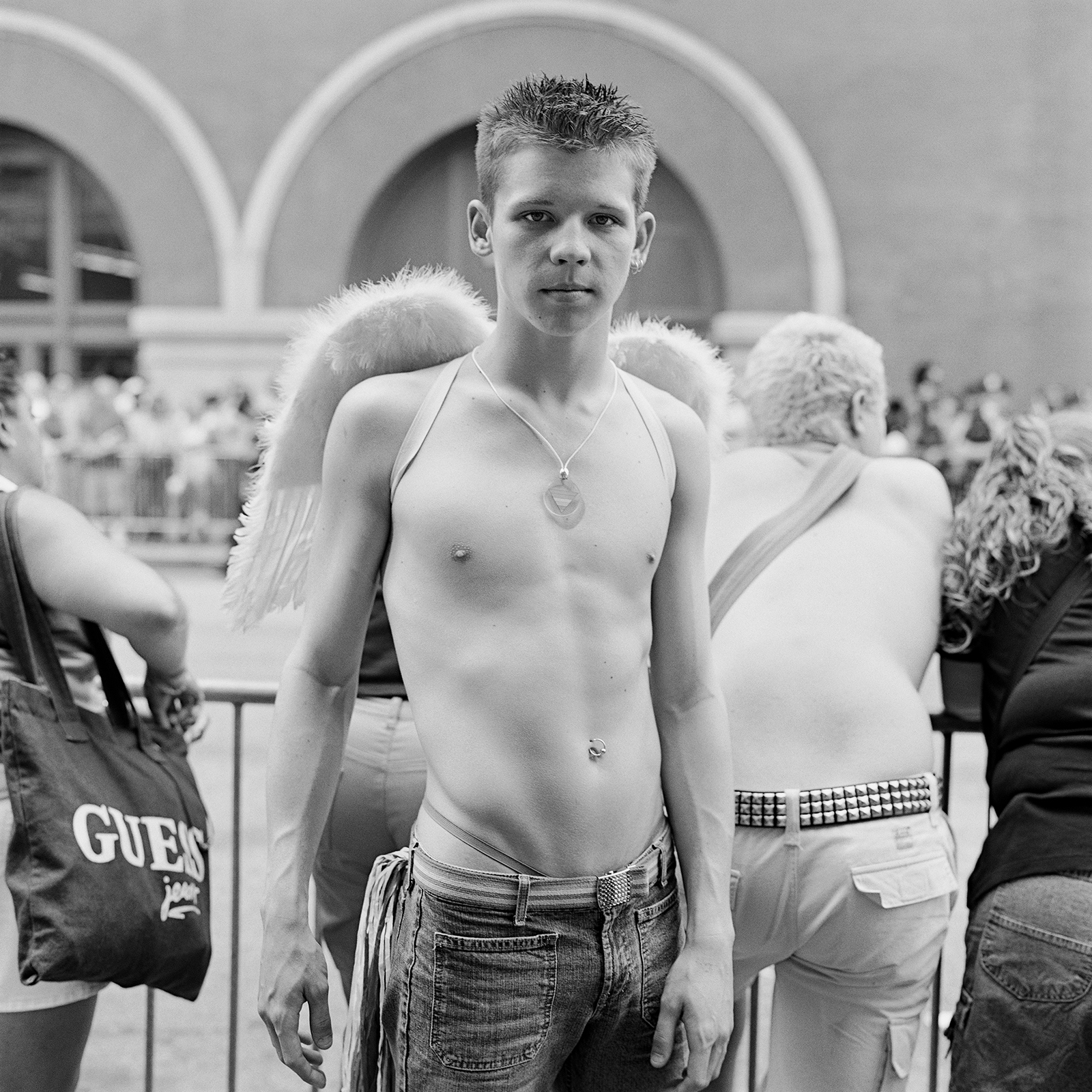 a topless man wearing angel wings and a necklace at a parade