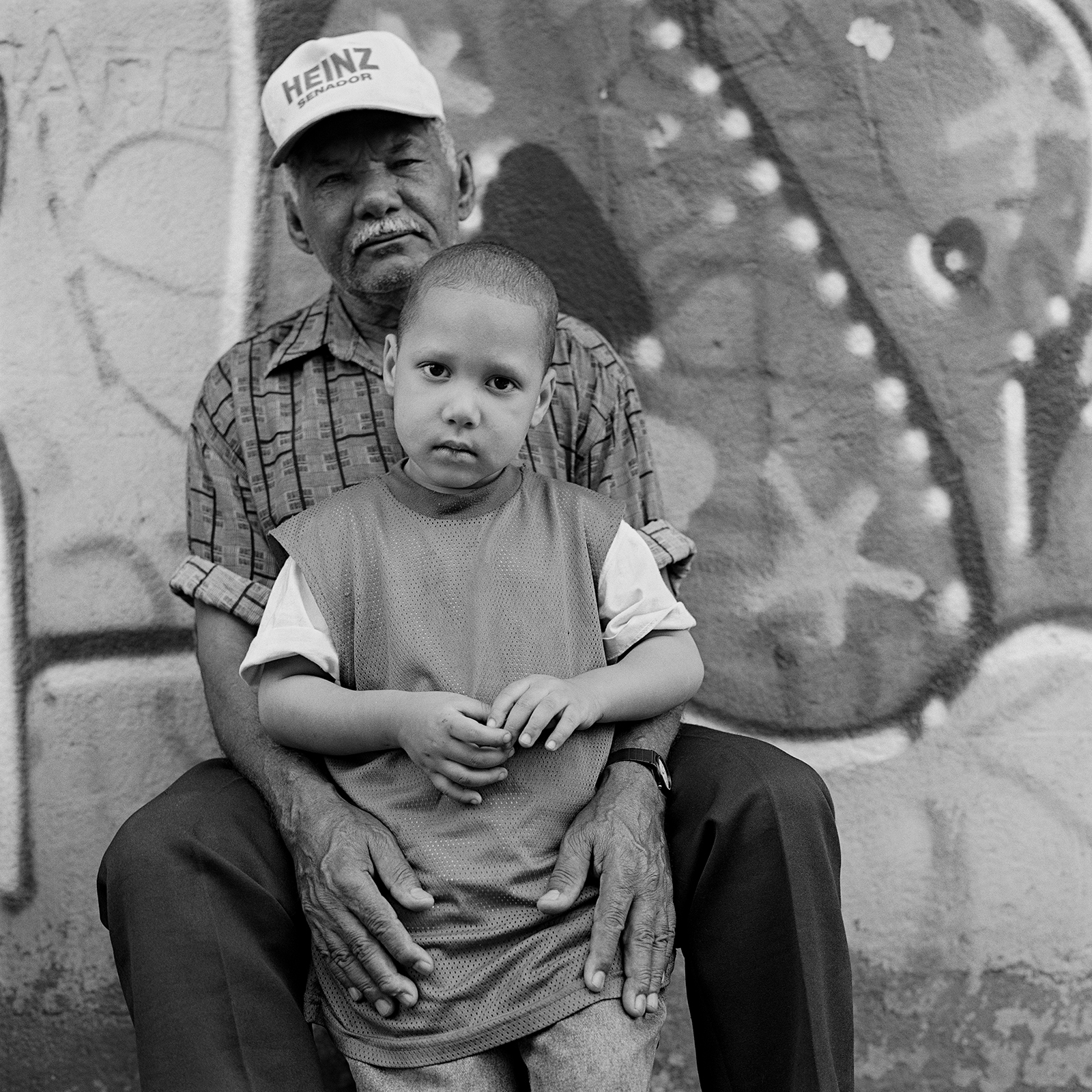 a man wearing a cap that reads 'heinz' holds a young boy between his legs