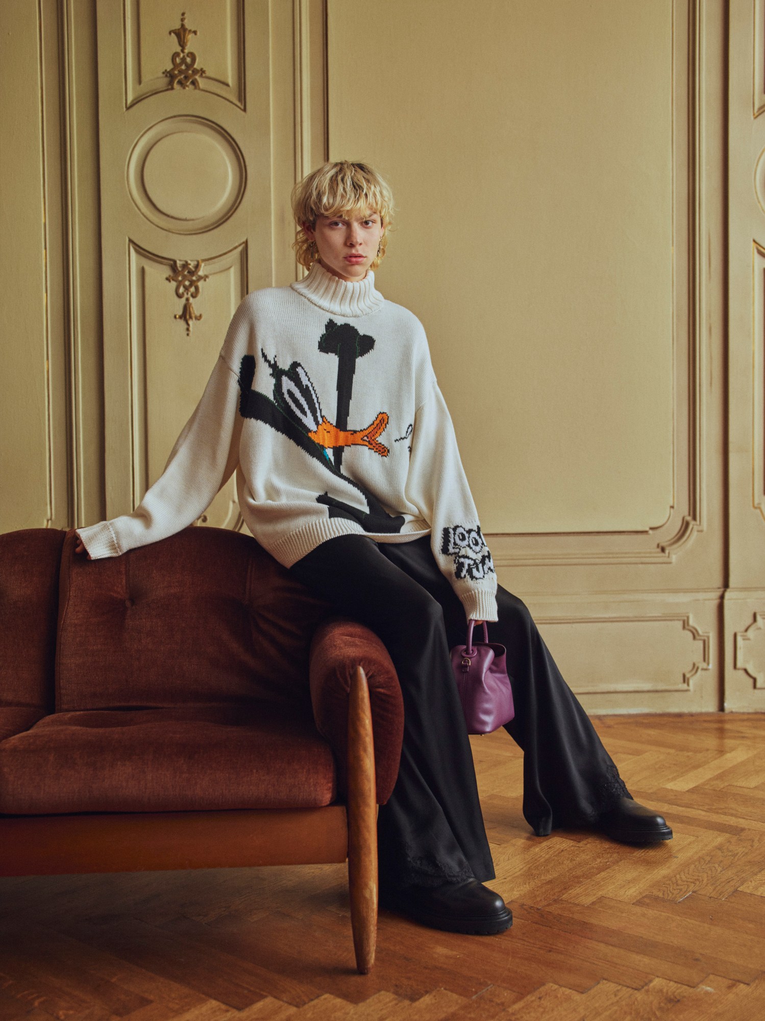 model wearing looney tunes sweater perched on a sofa by coco capitan