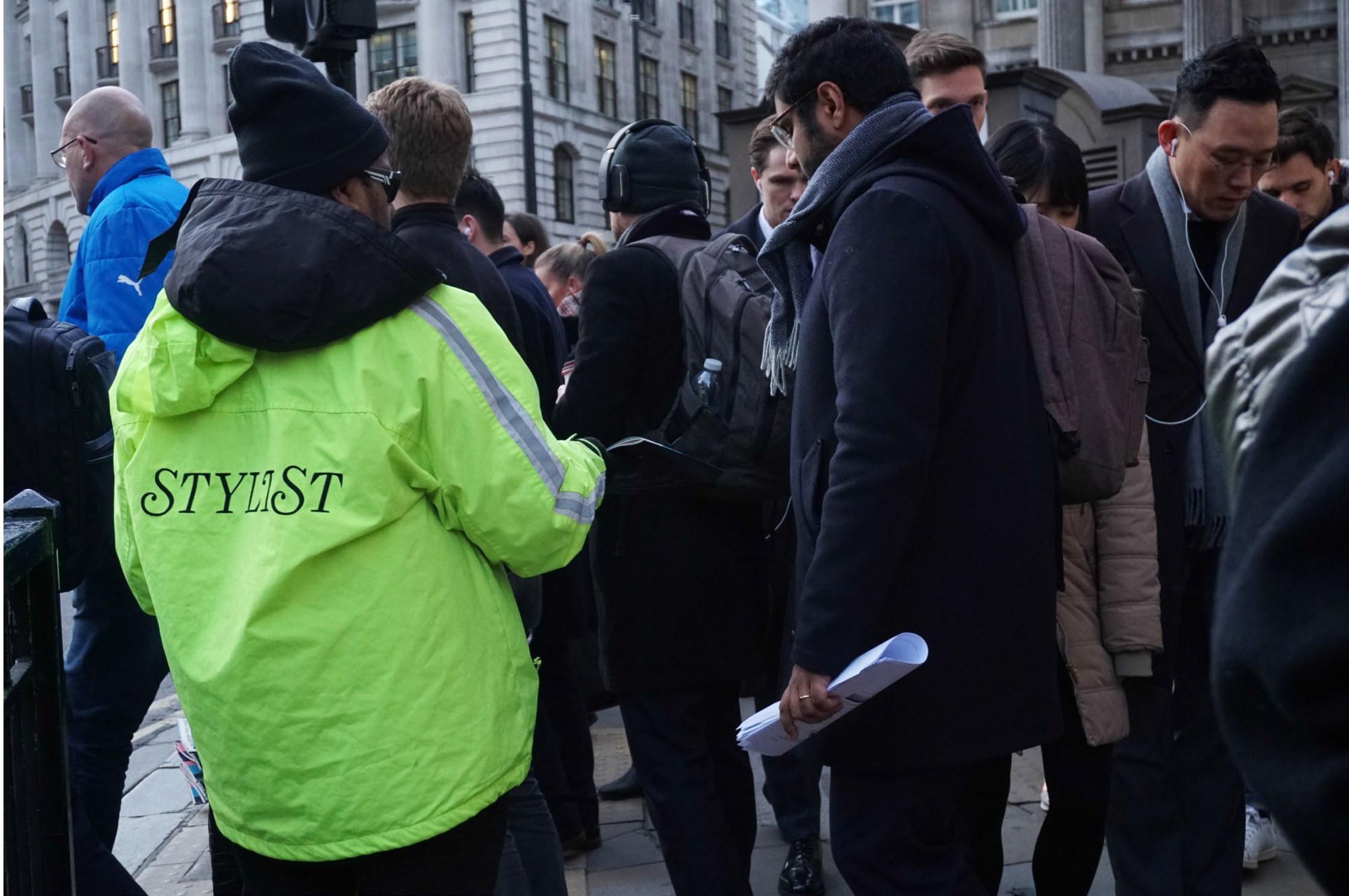 a man in a high vis jacket handing out magazines on a busy street