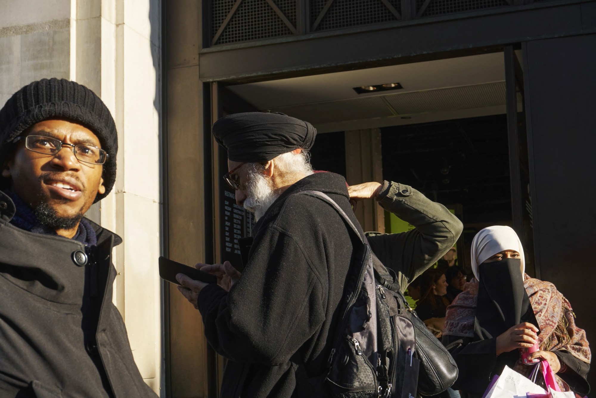 a man in a beanie hat looks into the camera as an older man looks away at his phone