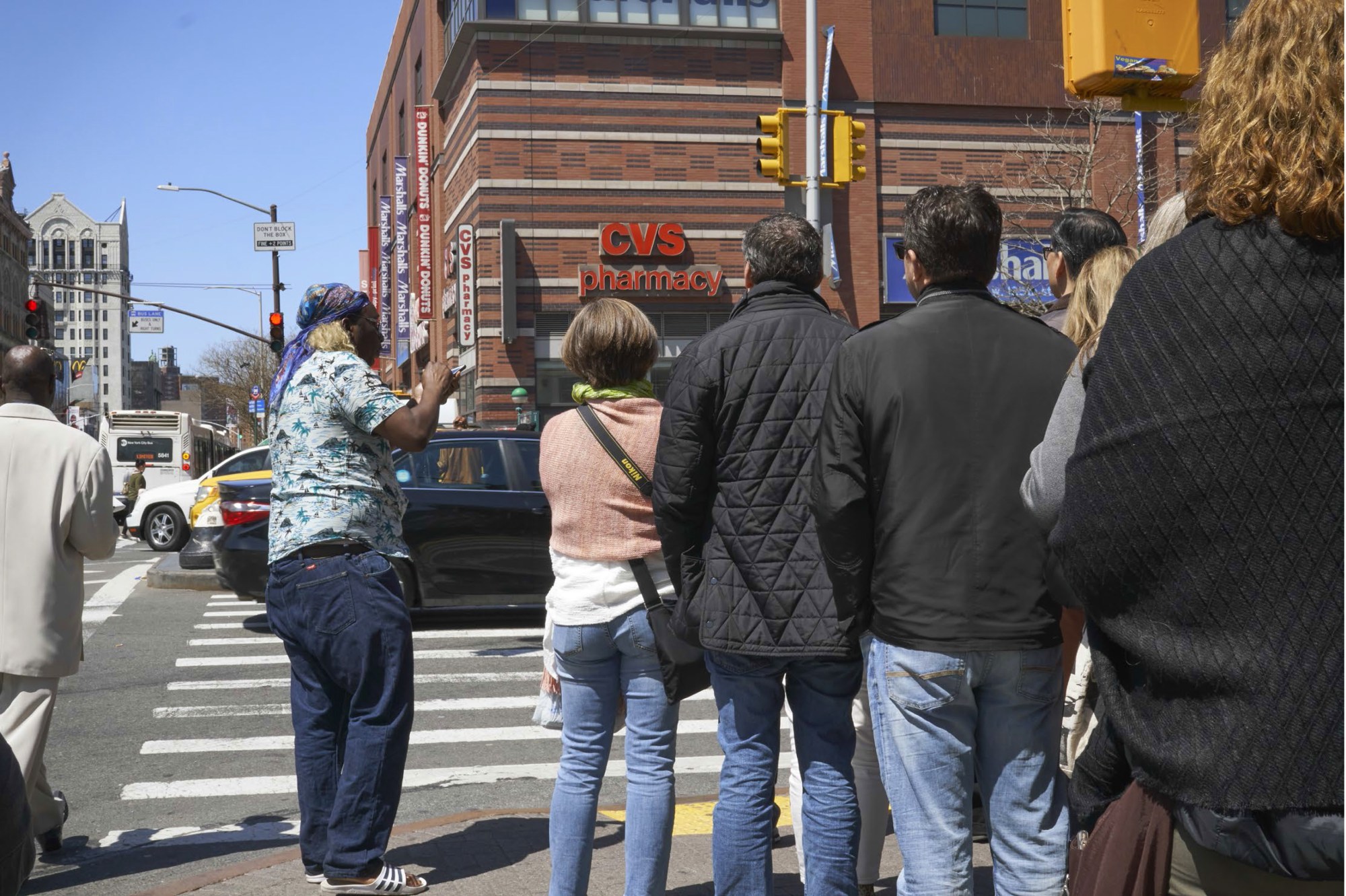 a man stands on the pavement by a crossing talking to strangers walking past