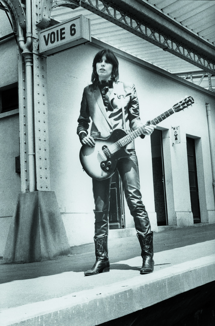 a photo of chrissie hynde from the pretenders holding a guitar at the train station by pierre rene-worms