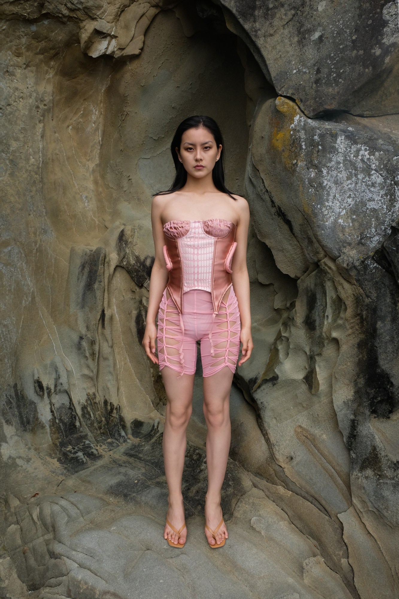 a model posing on a rock wearing a corset and cutout shorts by ORIENS