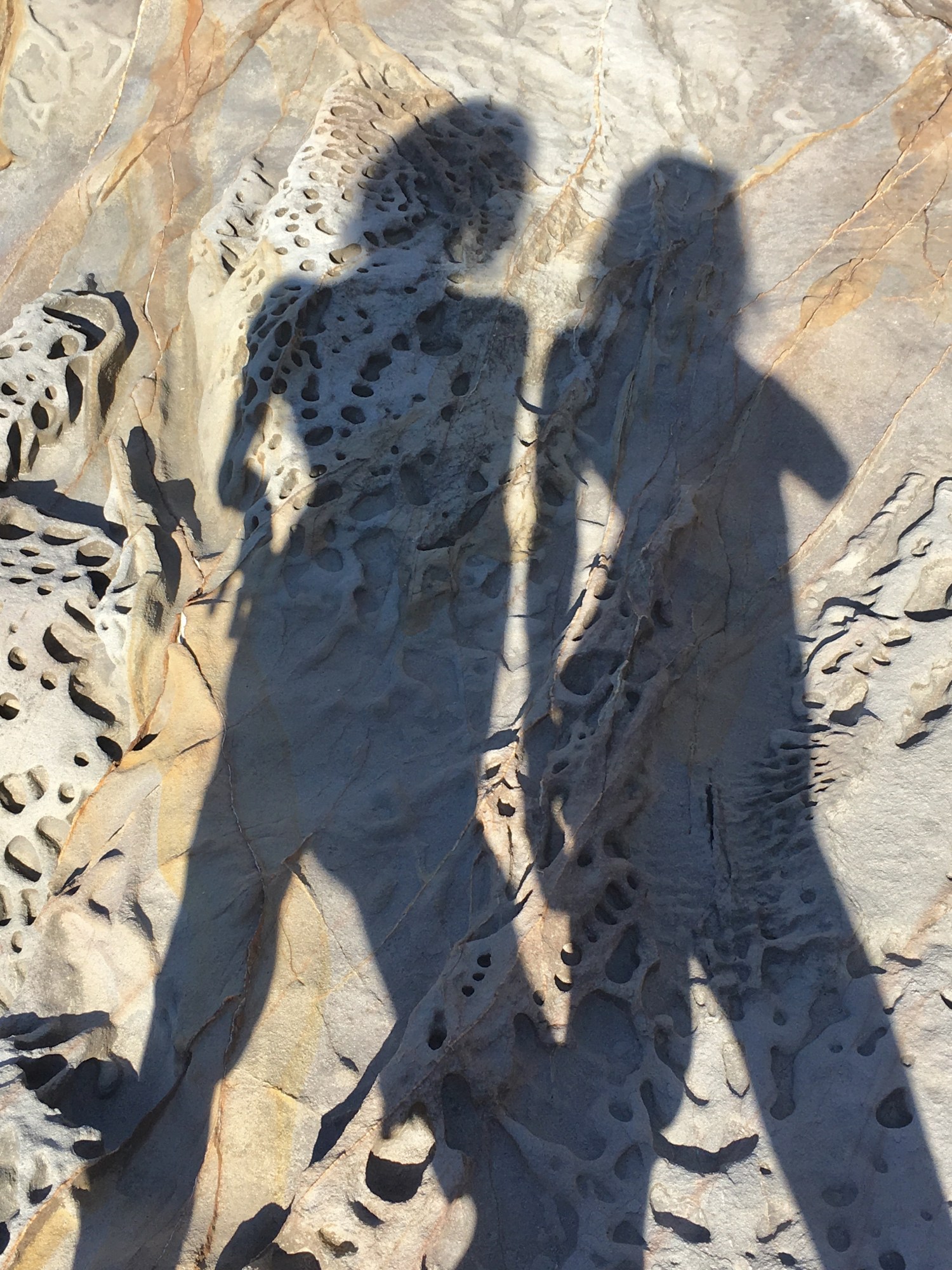 two near-identical female shadows on bumpy greyscale rocks full of holes