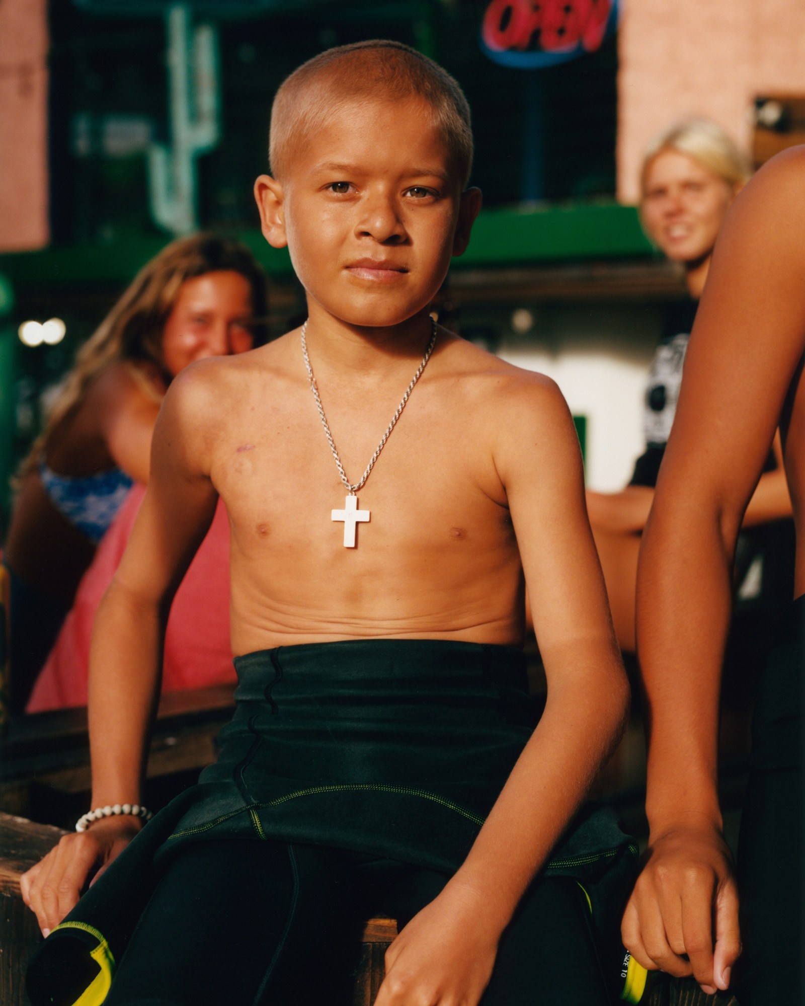 a young boy wearing a surf suit and a crucifix necklace