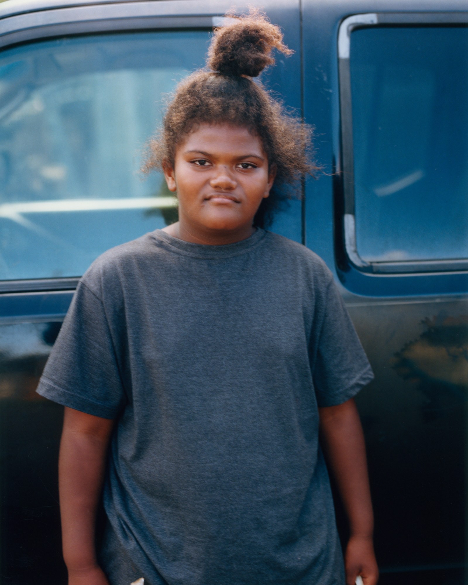 a young girl in a dark grey t-shirt stood in front of a car