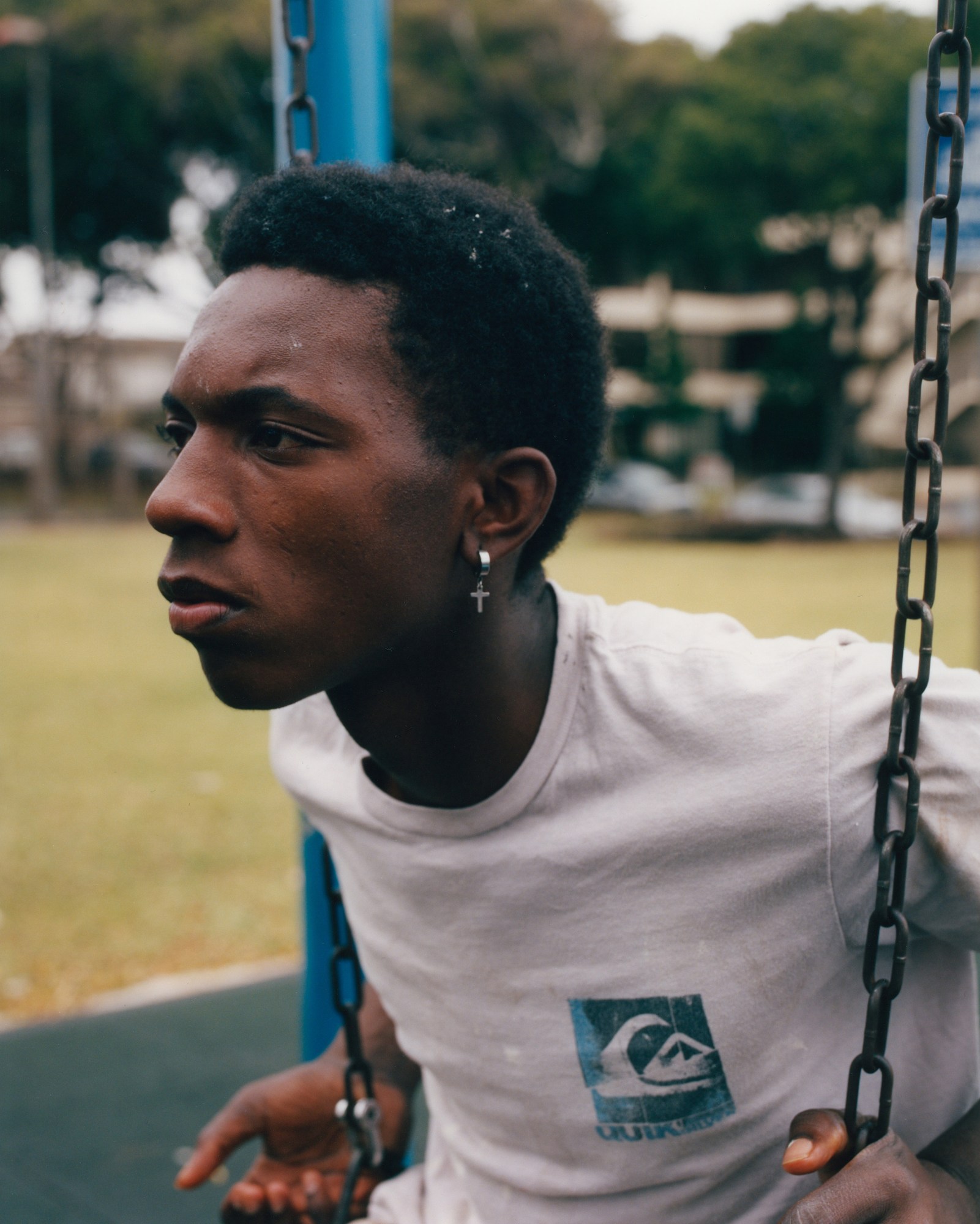 a young man with a cross earring and a quicksilver t-shirt sits on a swing