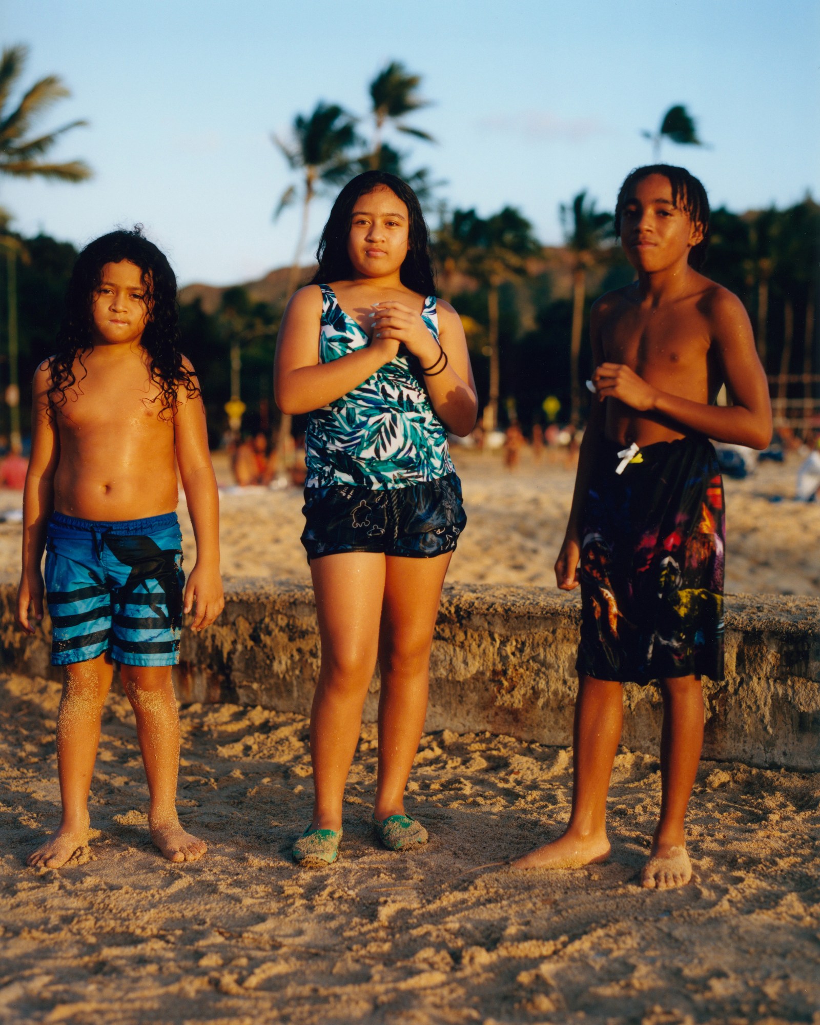 three young kids stand on the beach in a golden sunset light