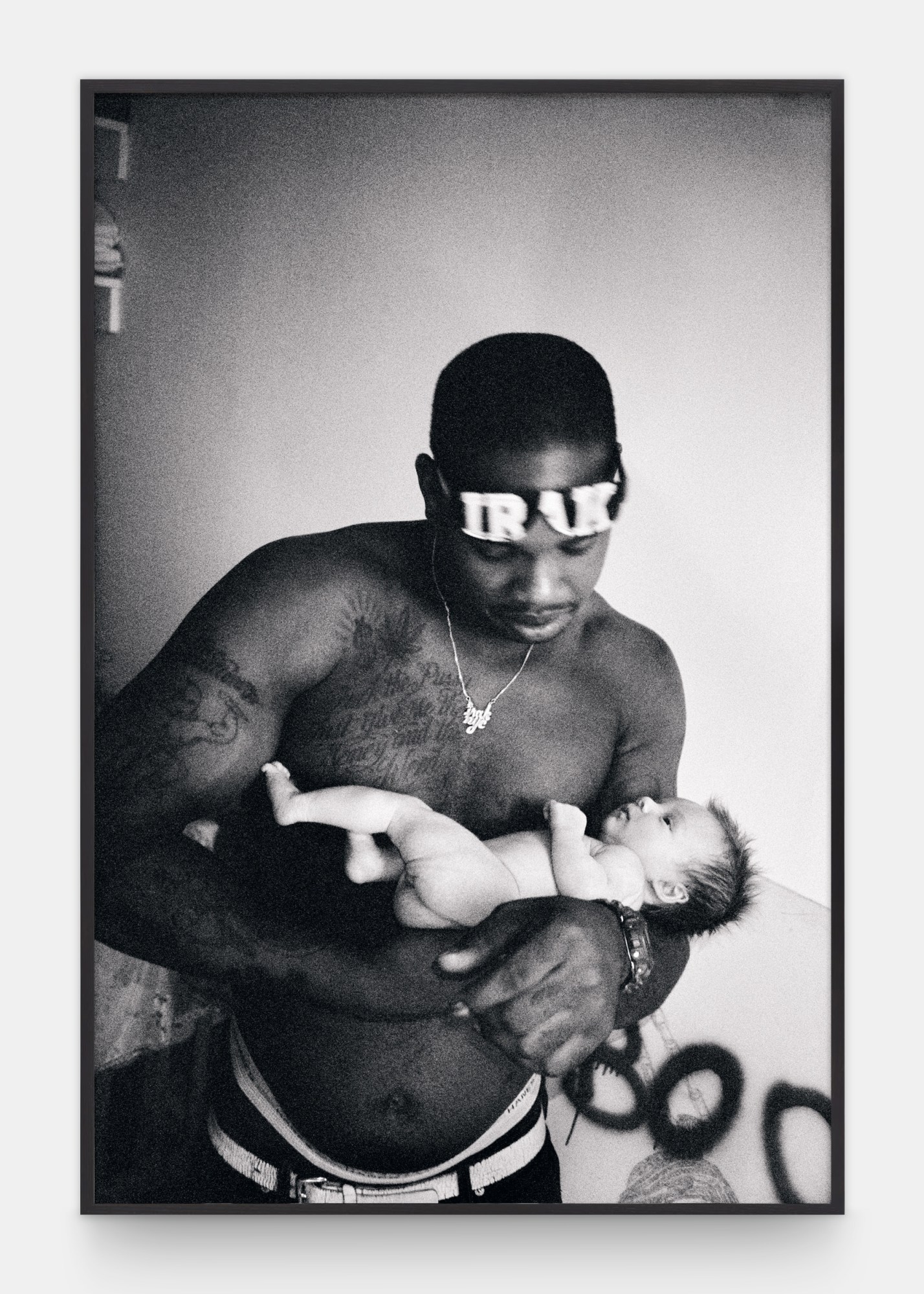 a topless man wearing an 'irak' headband holds a baby in his arms