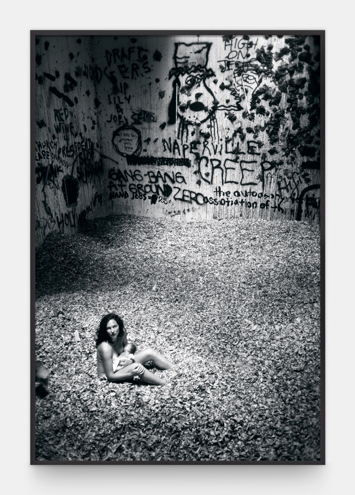 a naked woman breastfeeds a baby in a graffiti covered concrete space