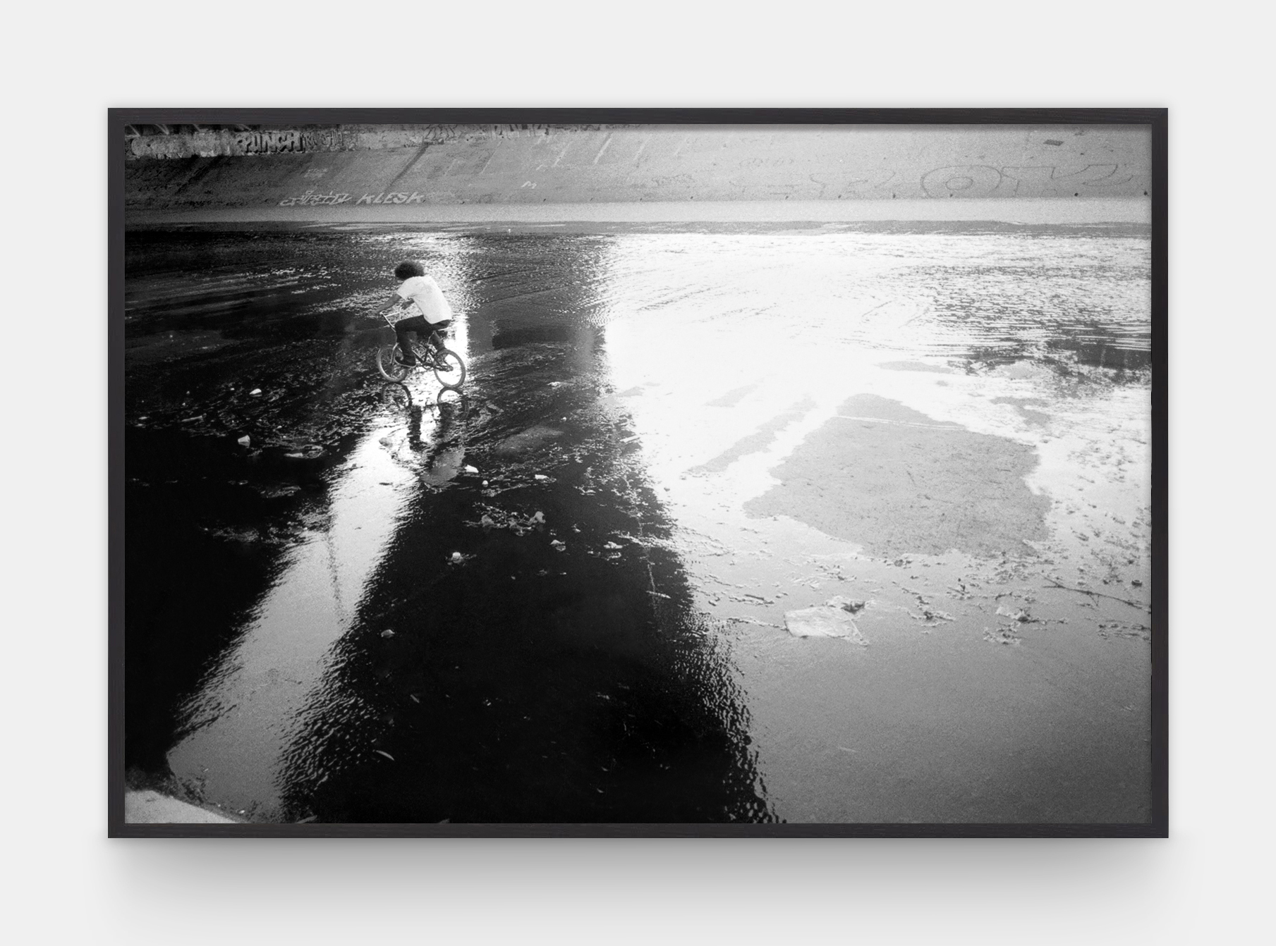 a man riding a bike across a wet concrete space